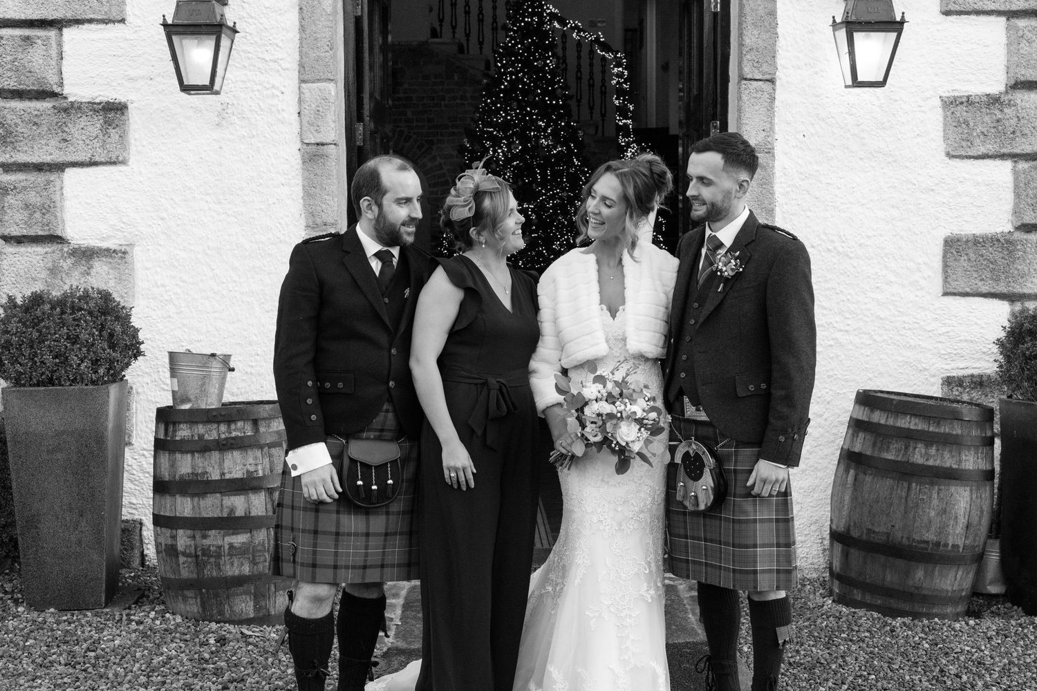 Wedding group photos with Scottish formal wear against white stone building and lanterns.