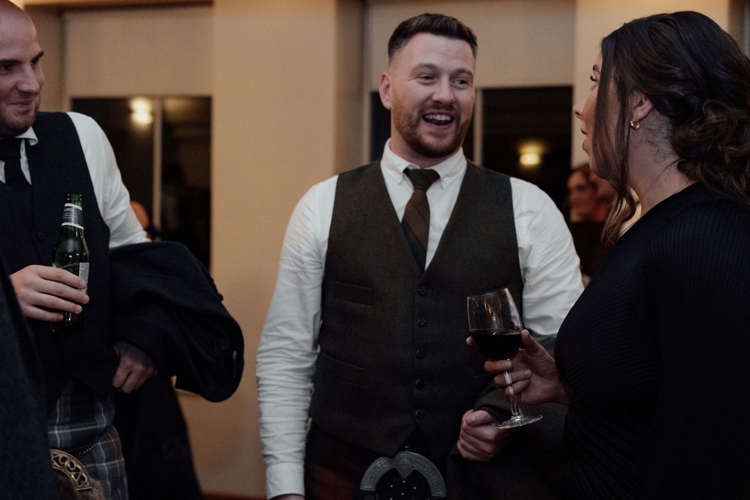 Guests in formal attire mingle and enjoy drinks during an evening wedding reception.