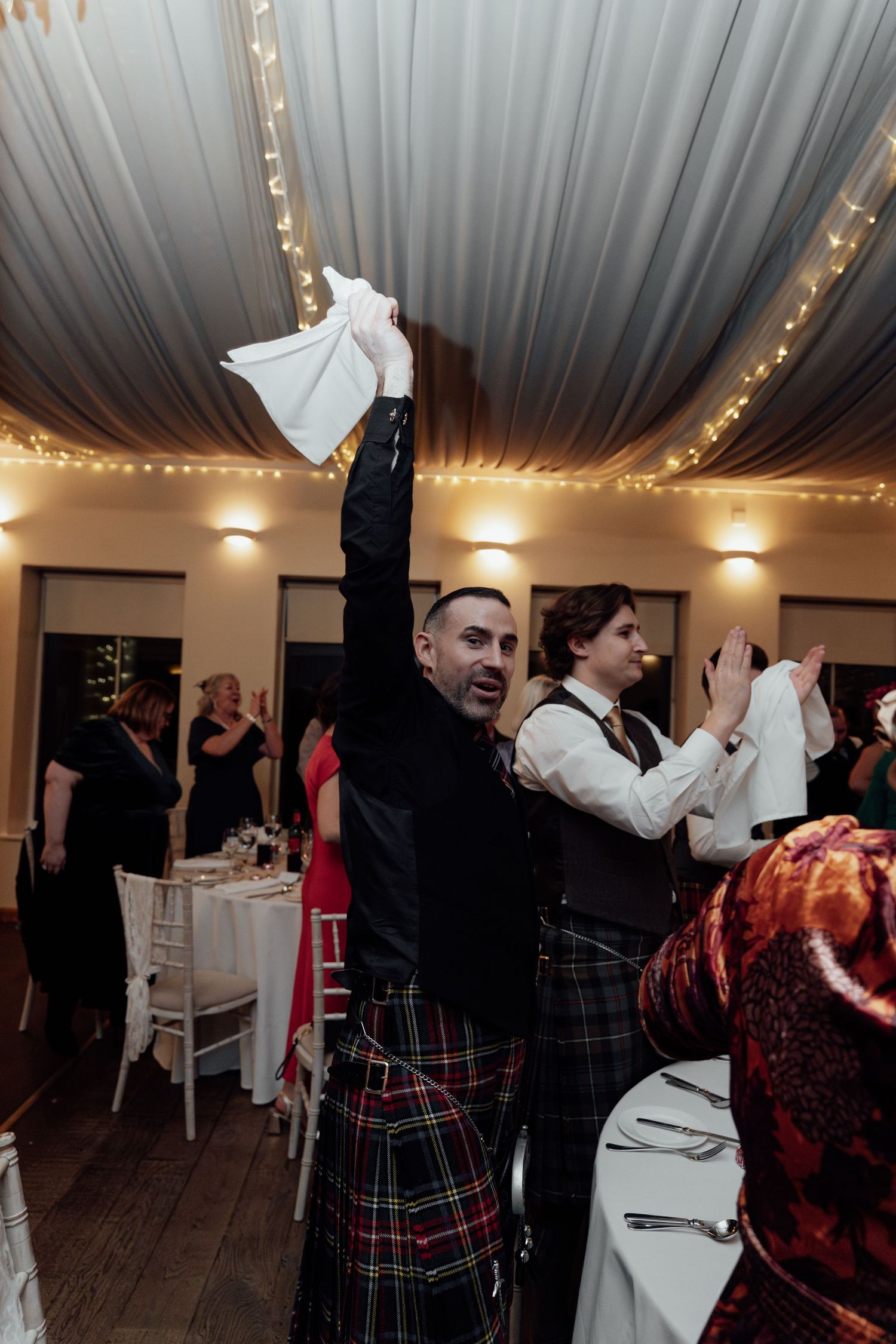 Wedding celebration with guests dancing under white draped ceiling adorned with string lights.
