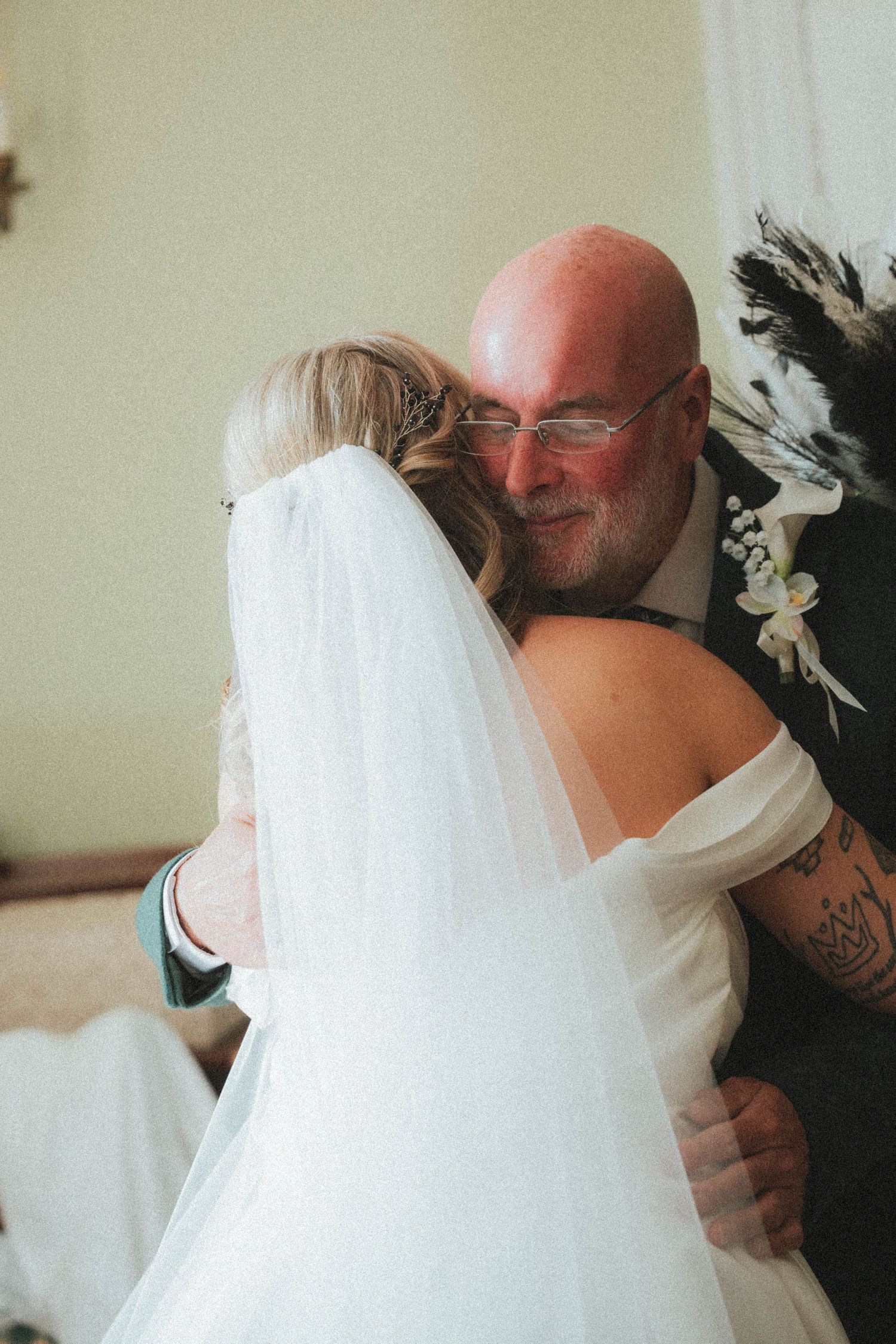 Emotional father hugging bride in white wedding dress and veil before ceremony.