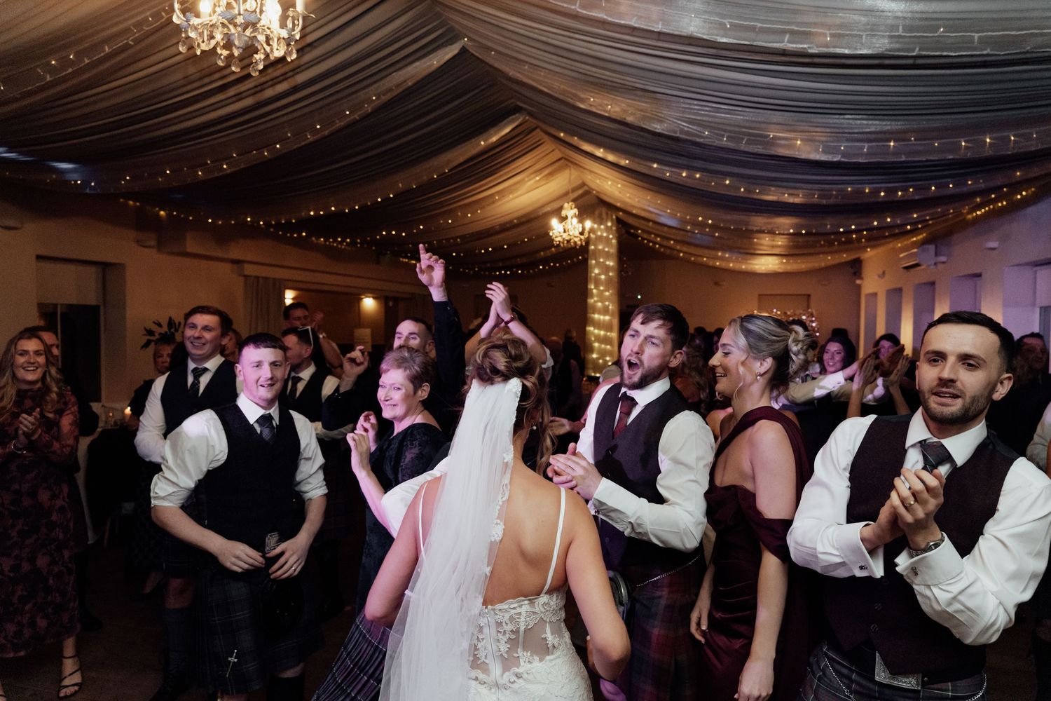Wedding reception dance floor filled with guests celebrating under elegant draped ceiling.