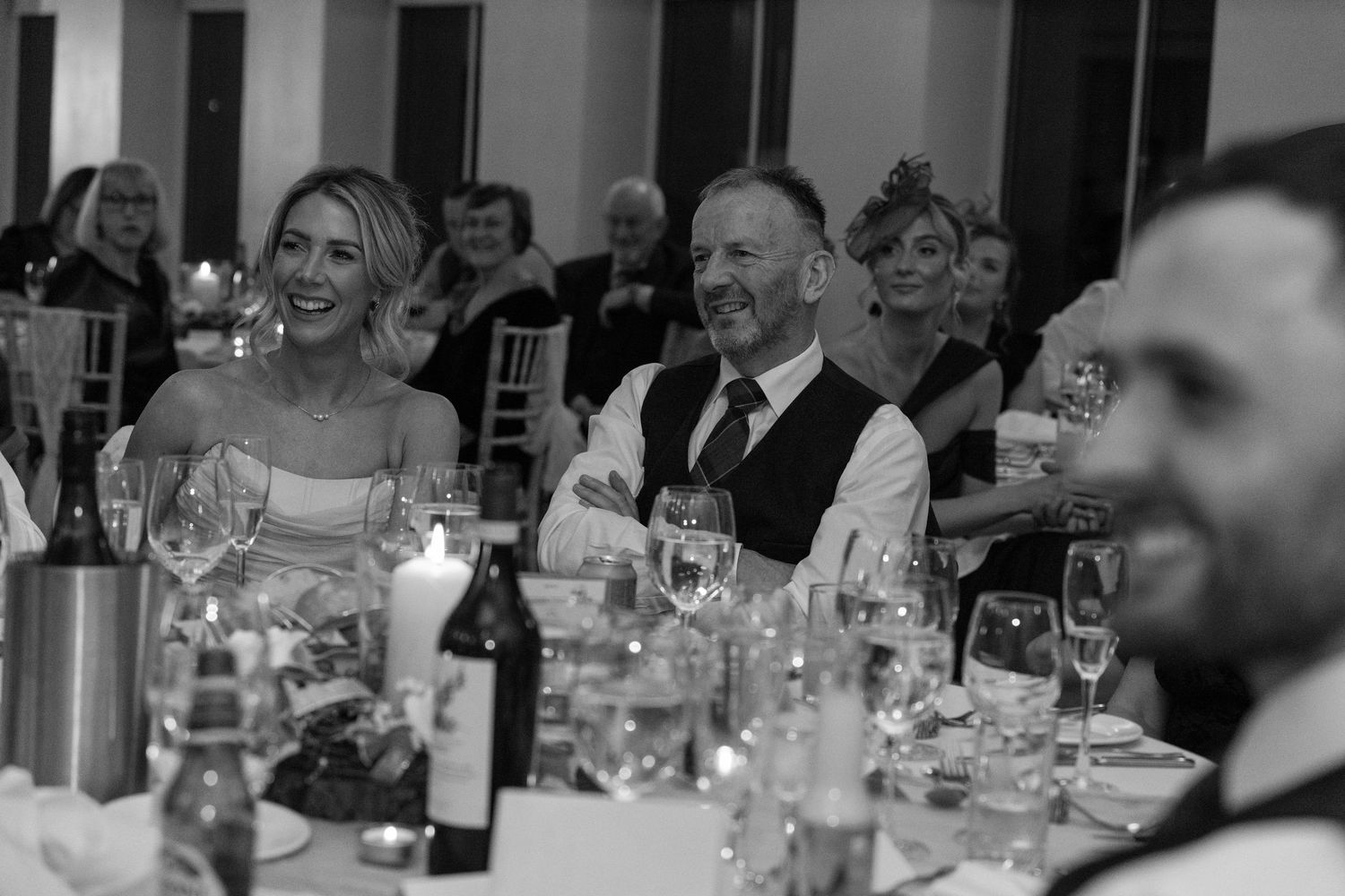 Black and white photo of wedding guests sharing joyful moments during reception dinner.