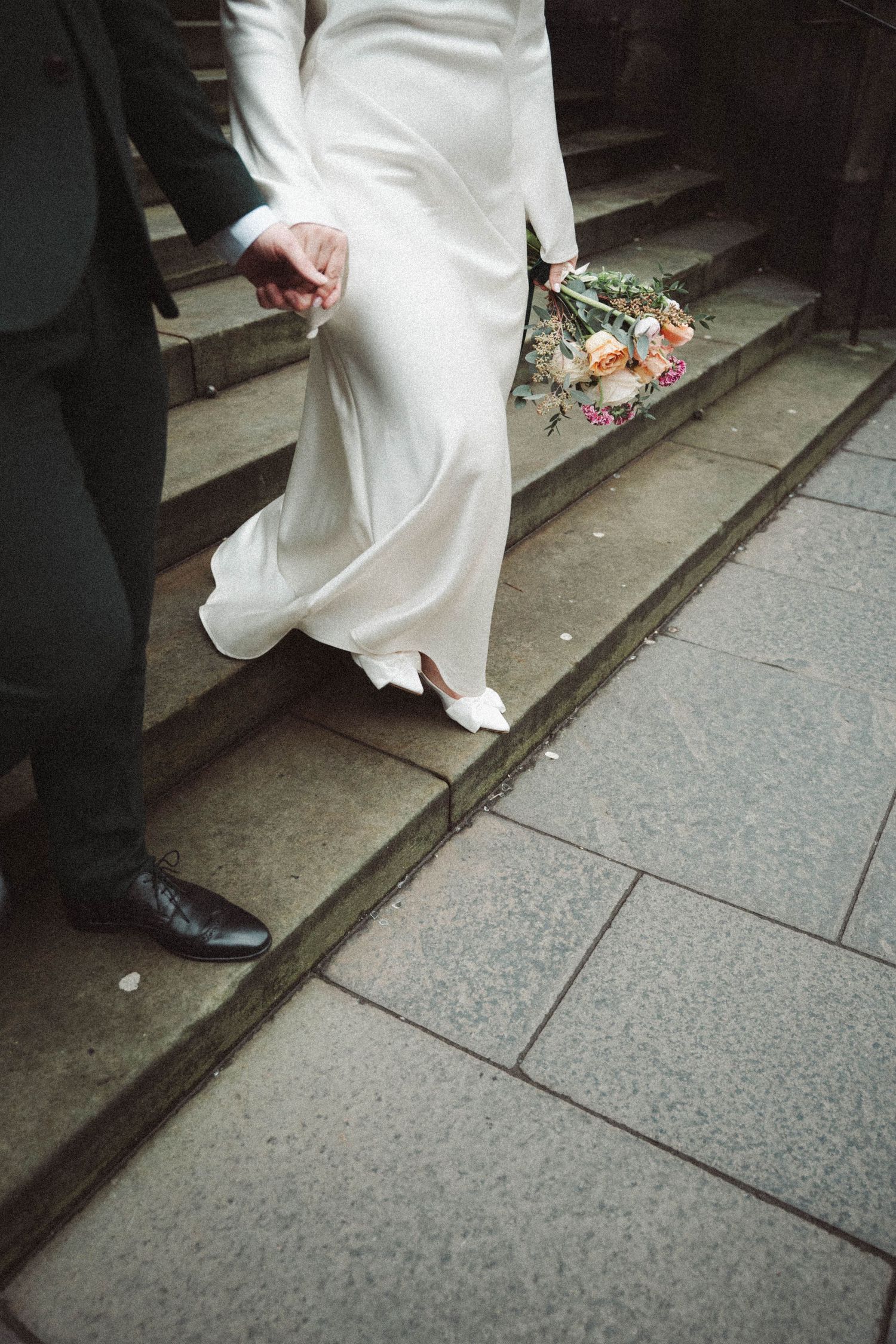 White wedding dress hem and dress shoes walking down stone steps.