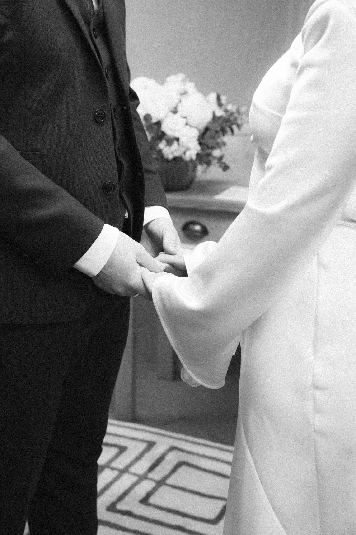 Black and white photo of formal wedding attire details and clasped hands.