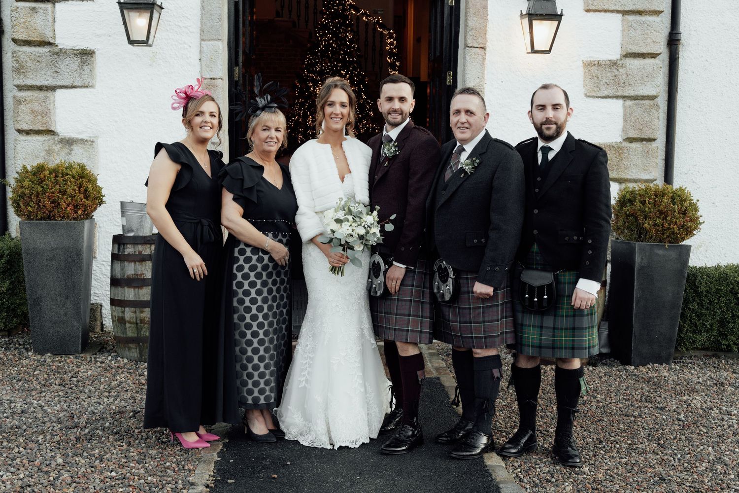 Wedding party members pose together outside a white building with lanterns.