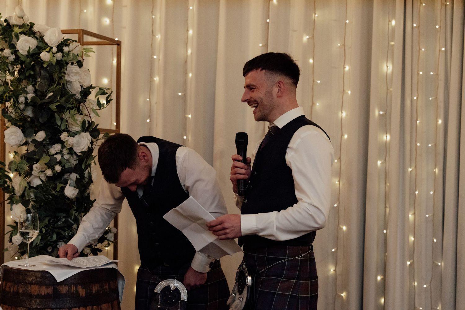 Wedding reception venue features romantic string light backdrop and white floral decorations.