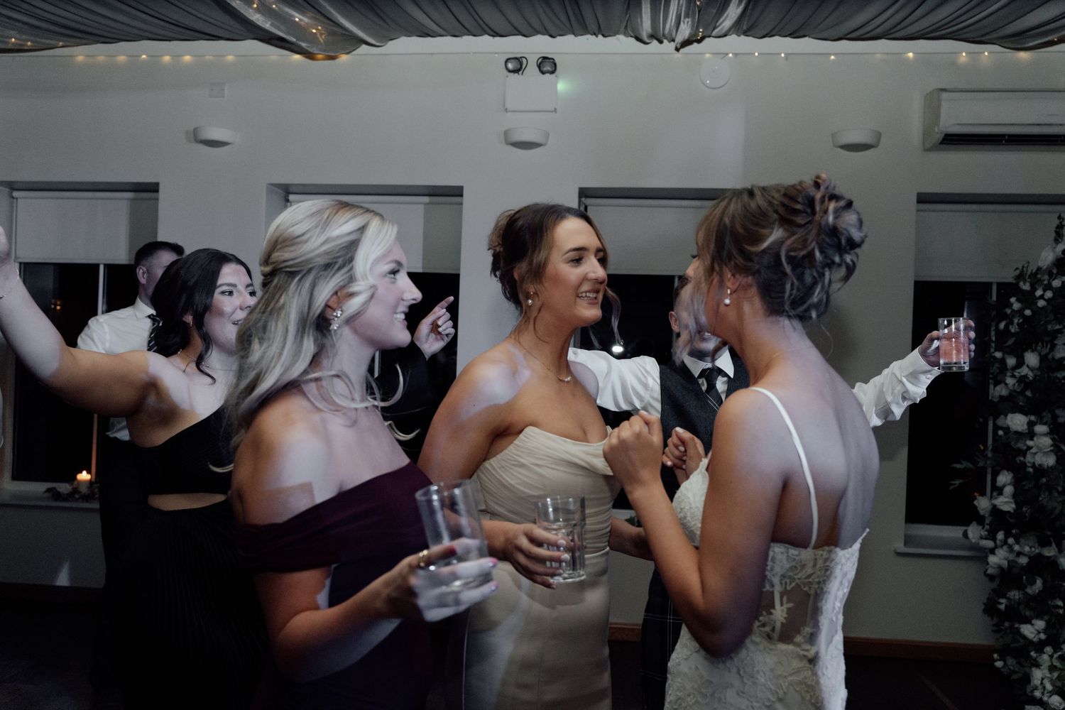 Wedding party members sharing drinks and laughter at indoor reception venue.