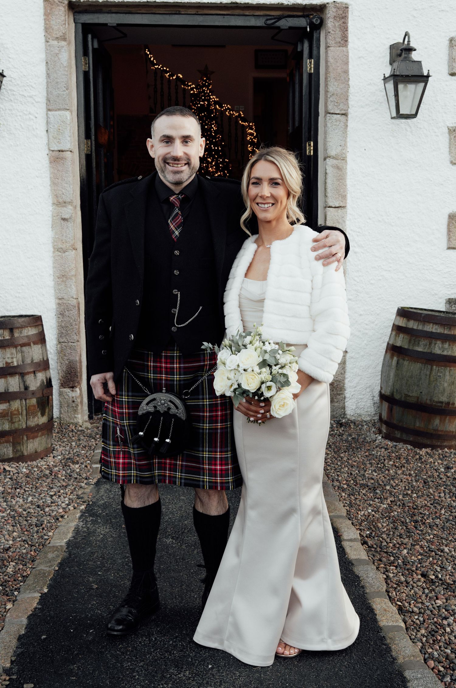 Candid wedding photo showing Scottish formal wear and white dresses outside stone building.