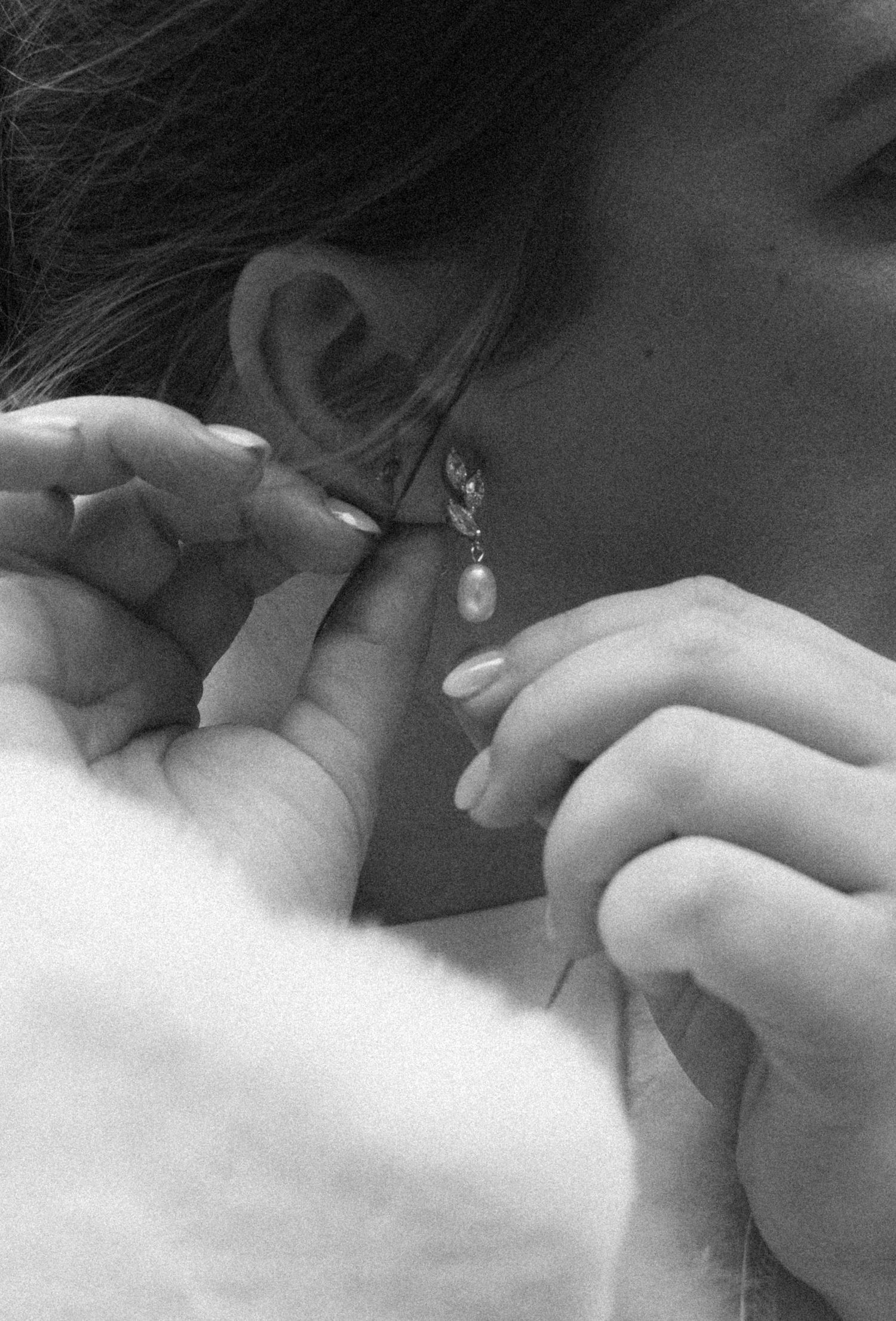 Close-up of hands fastening delicate jewelry in black and white.