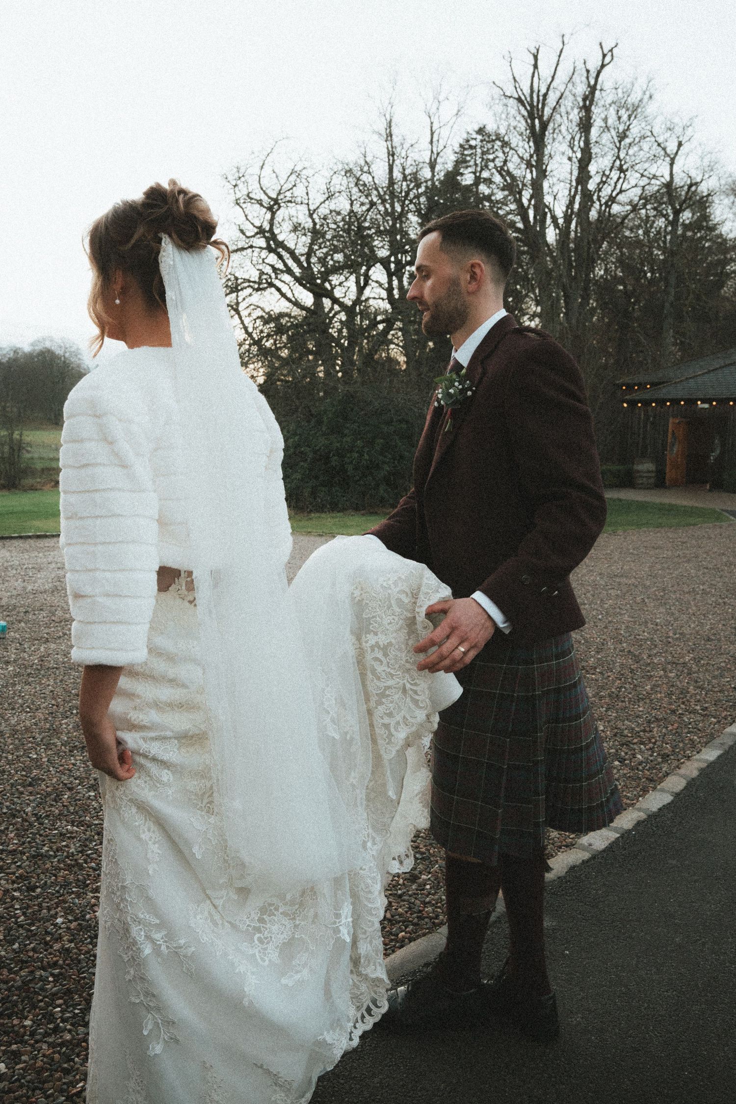 Wedding dress train being adjusted outdoors on a winter day near stone building entrance.