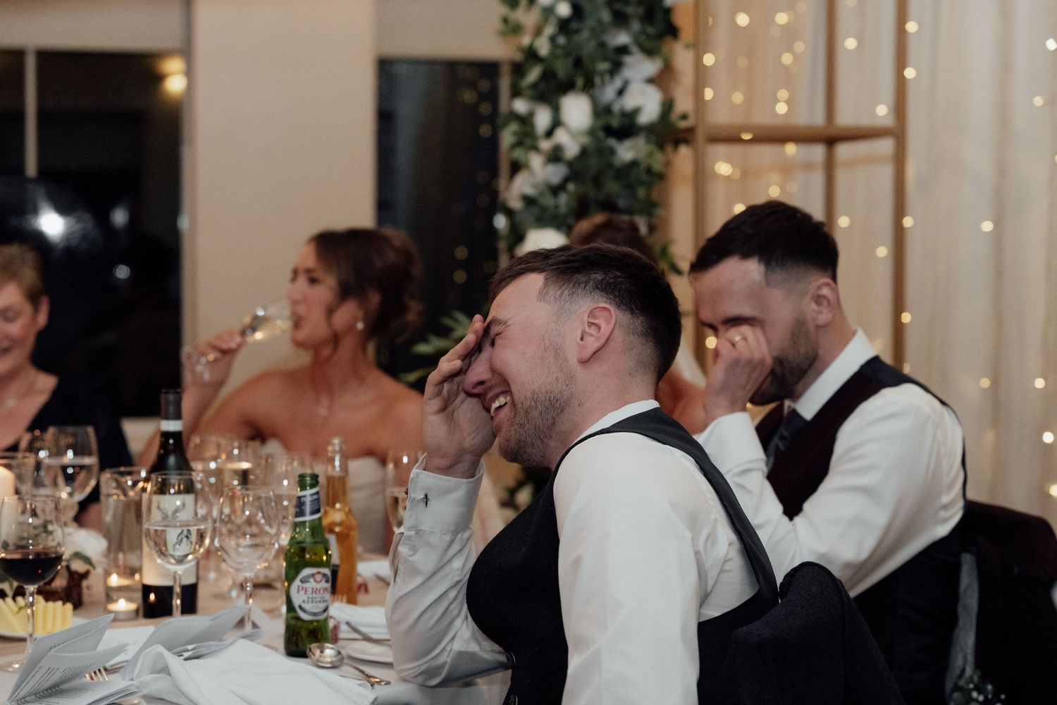 Wedding guests mingling and celebrating at decorated reception tables with floral arrangements.