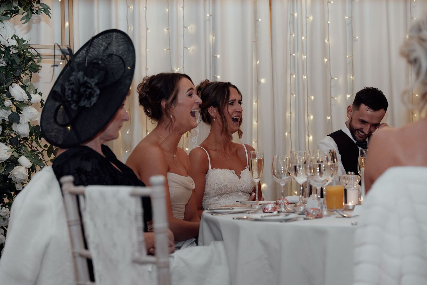 Wedding celebration with guests seated at decorated tables with fairy light backdrop.