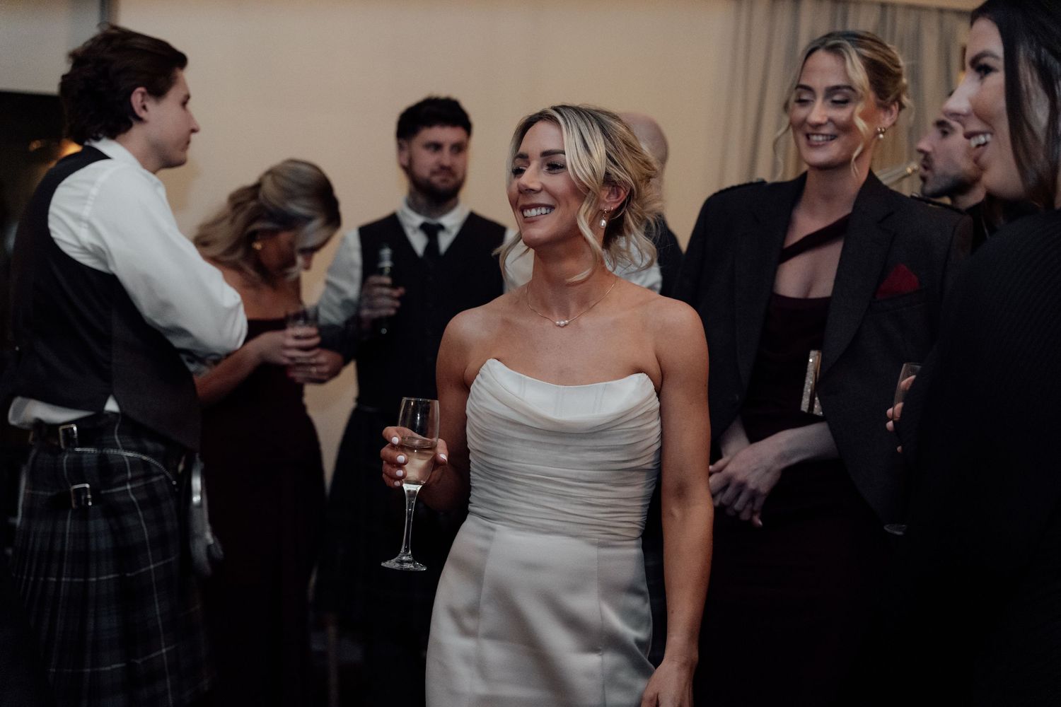 Wedding guests laugh and dance together during a reception celebration under warm lighting.