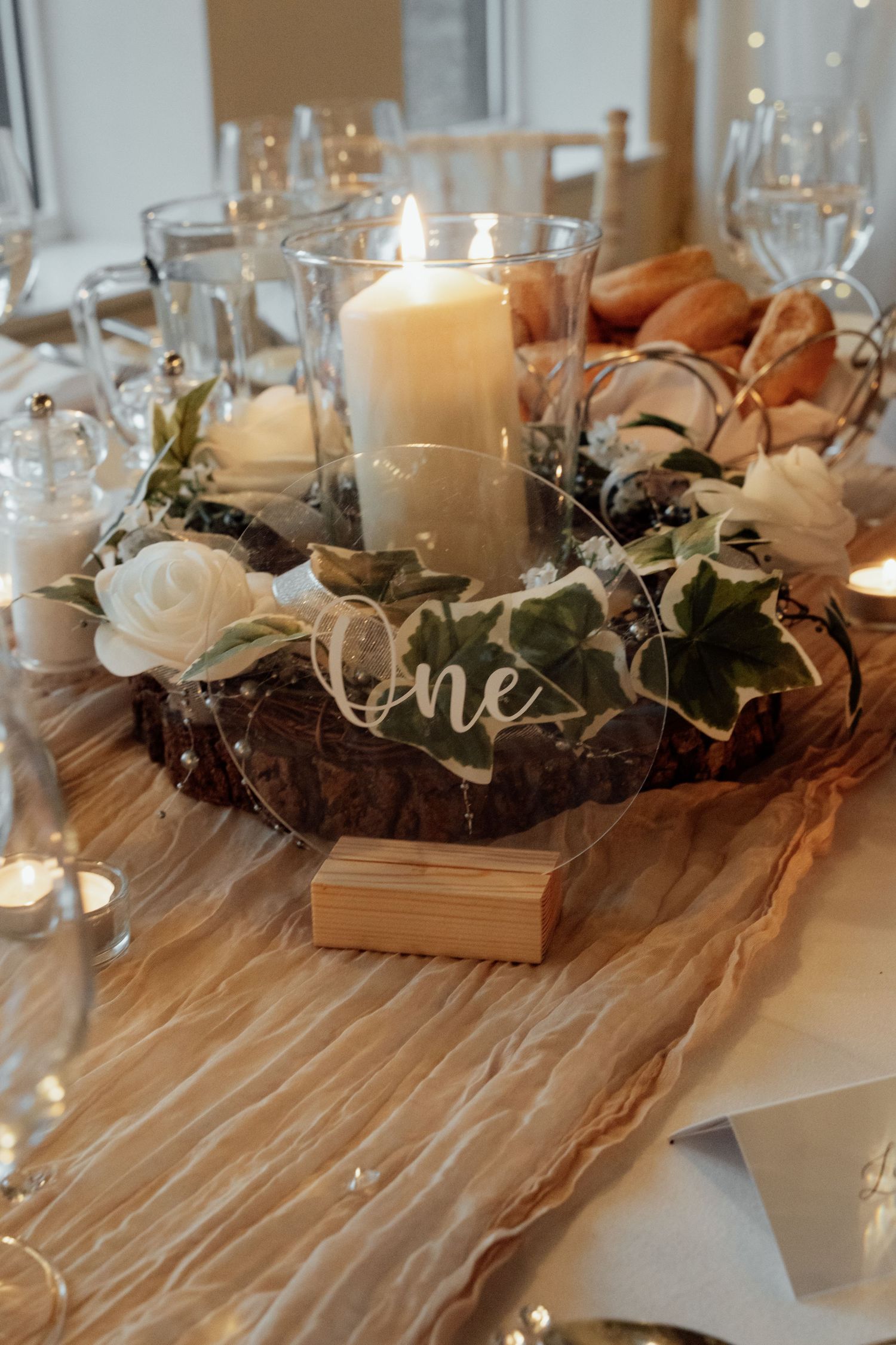 Romantic table centerpiece with candles, flowers and 'one' sign on champagne runner.
