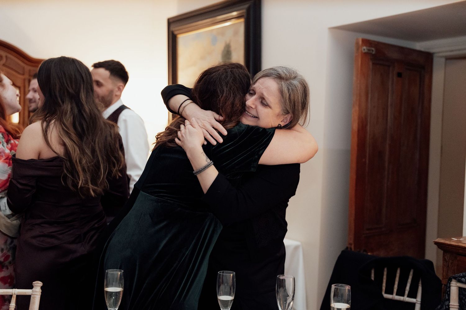 Guests sharing embraces and conversations at an indoor social event.