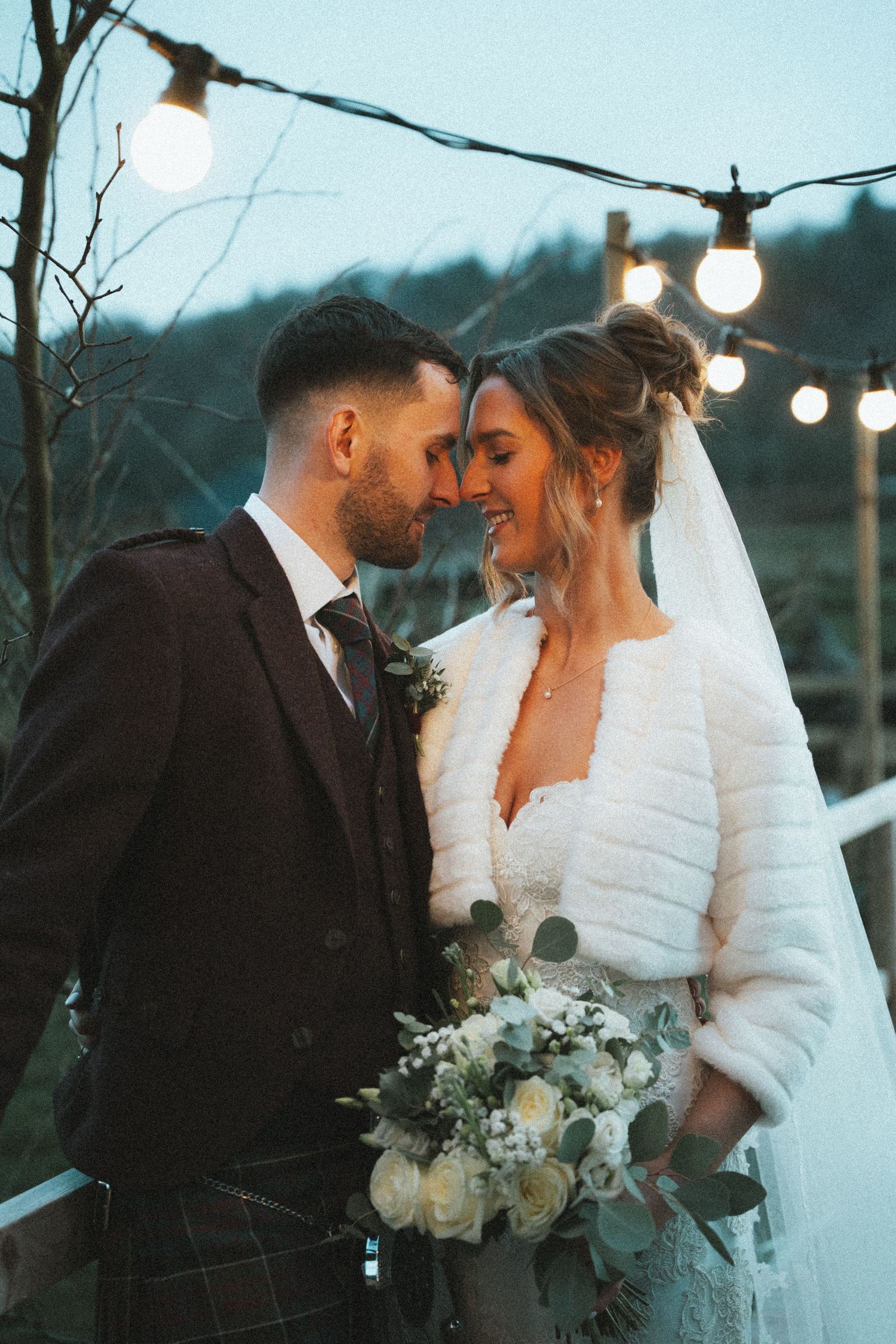 Romantic twilight wedding portrait with string lights creating soft ambiance.