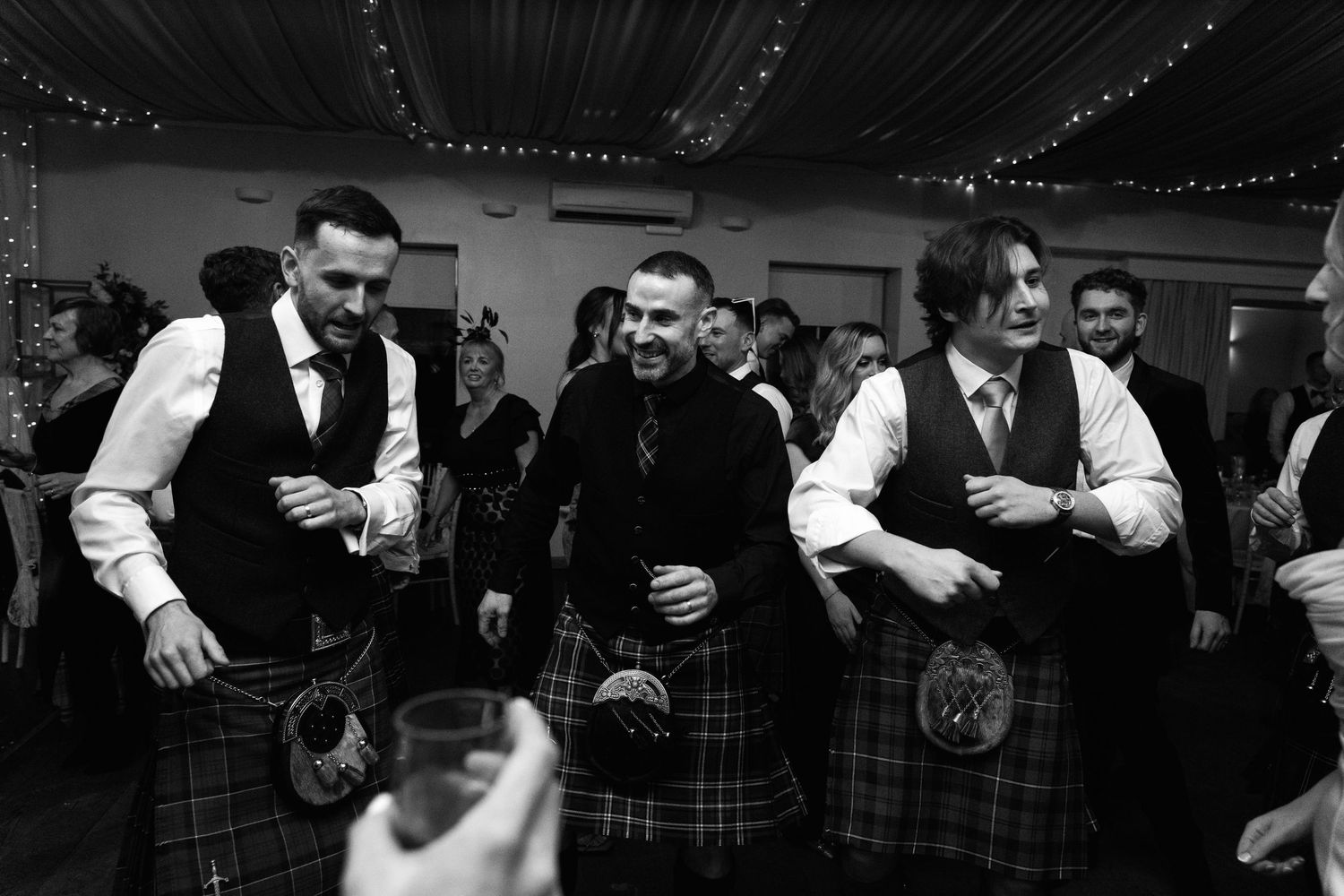 Men in traditional Scottish kilts gather during a festive wedding reception.