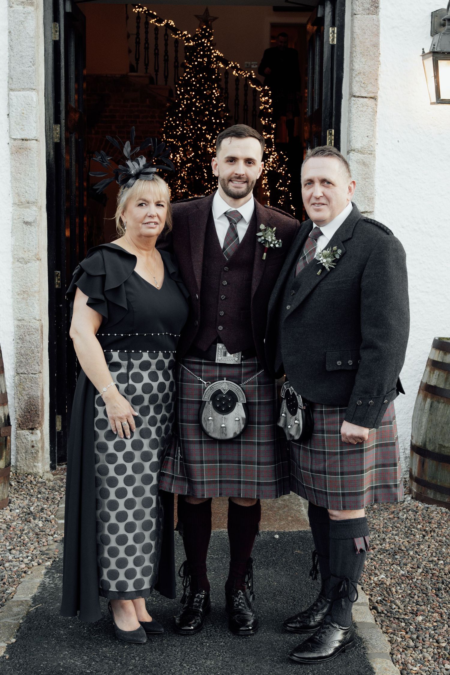 A group in formal attire including traditional Scottish kilts poses outside a building entrance.