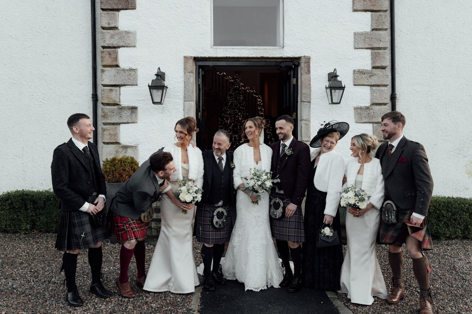 Wedding group portrait in front of historic white building with Scottish elements.