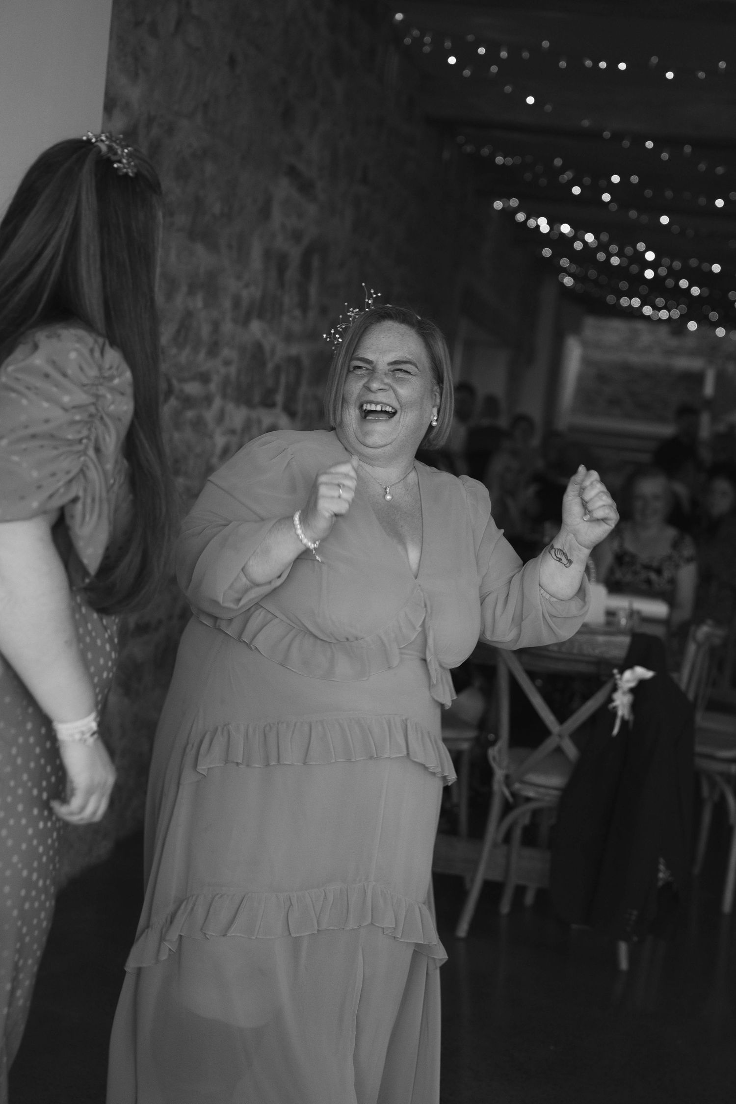 Black and white photo of a woman laughing and dancing joyfully at a wedding reception.
