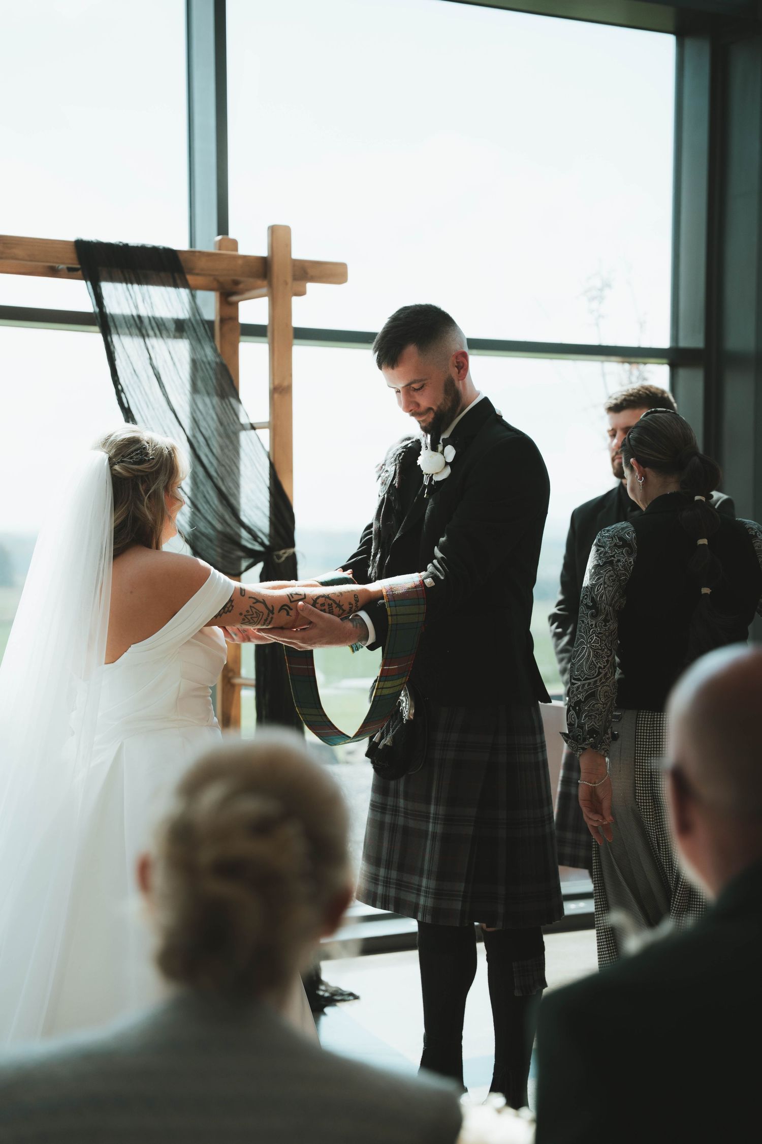 Groom in tartan kilt exchanging vows with bride at altar during Scottish wedding ceremony indoors.