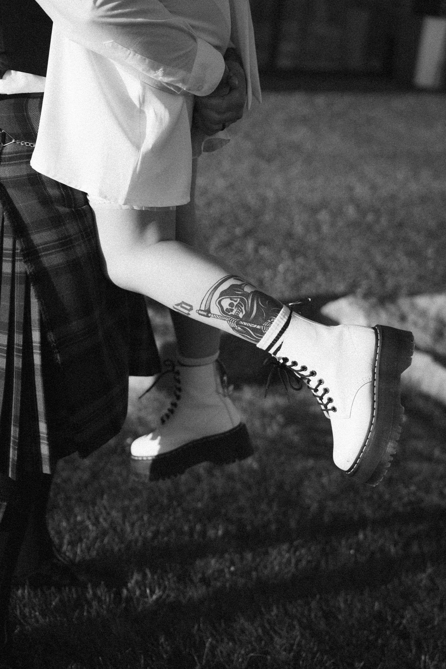 Close-up of bride wearing white Doc Martens boots with leg tattoo next to groom in tartan kilt.