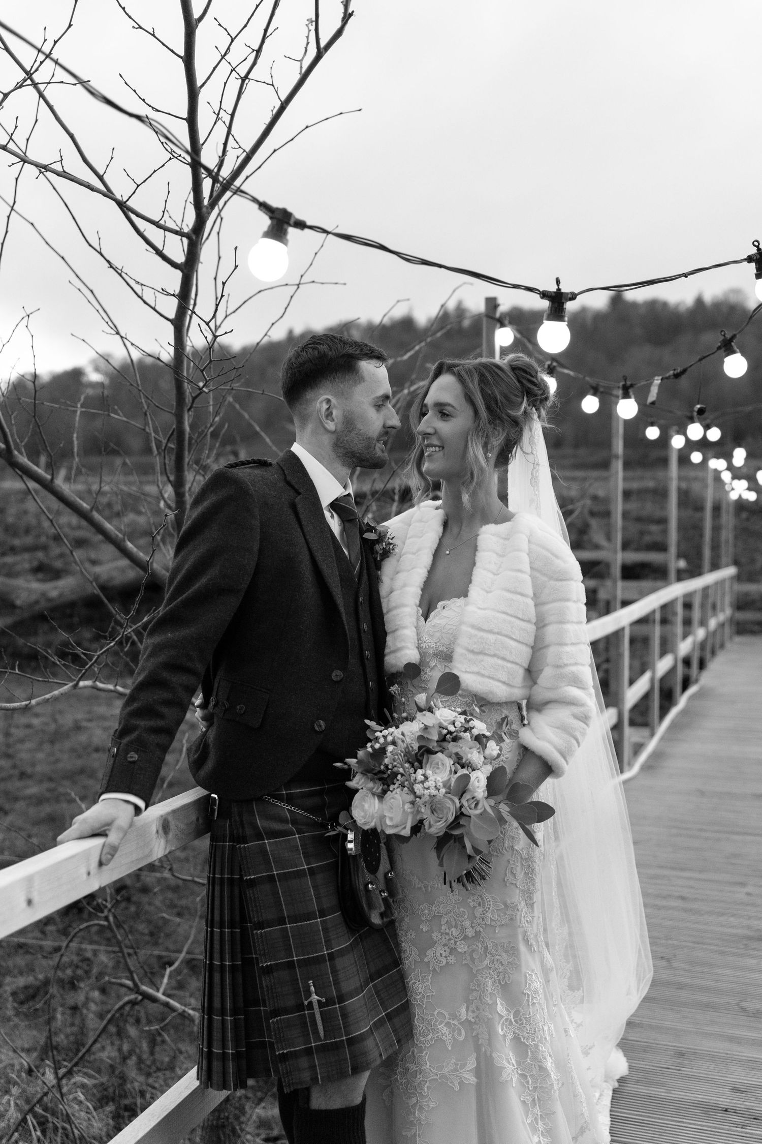 Wedding couple shares intimate moment on illuminated wooden bridge during twilight.