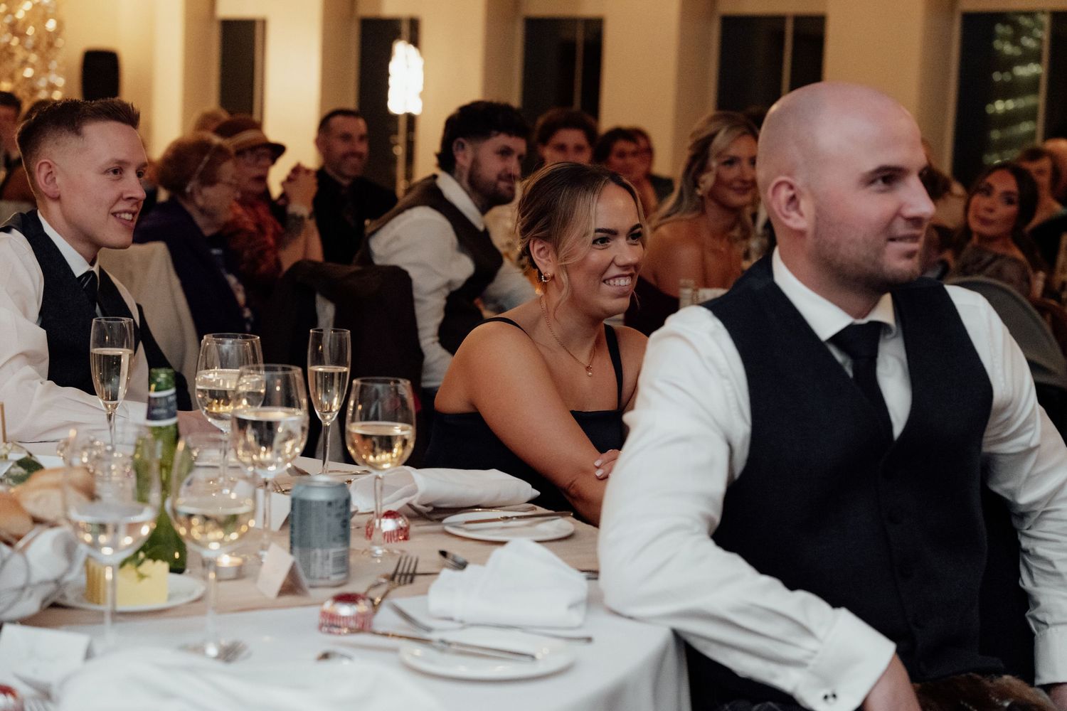 Formal dinner guests in black and white attire gathered around elegantly set tables at an evening event.
