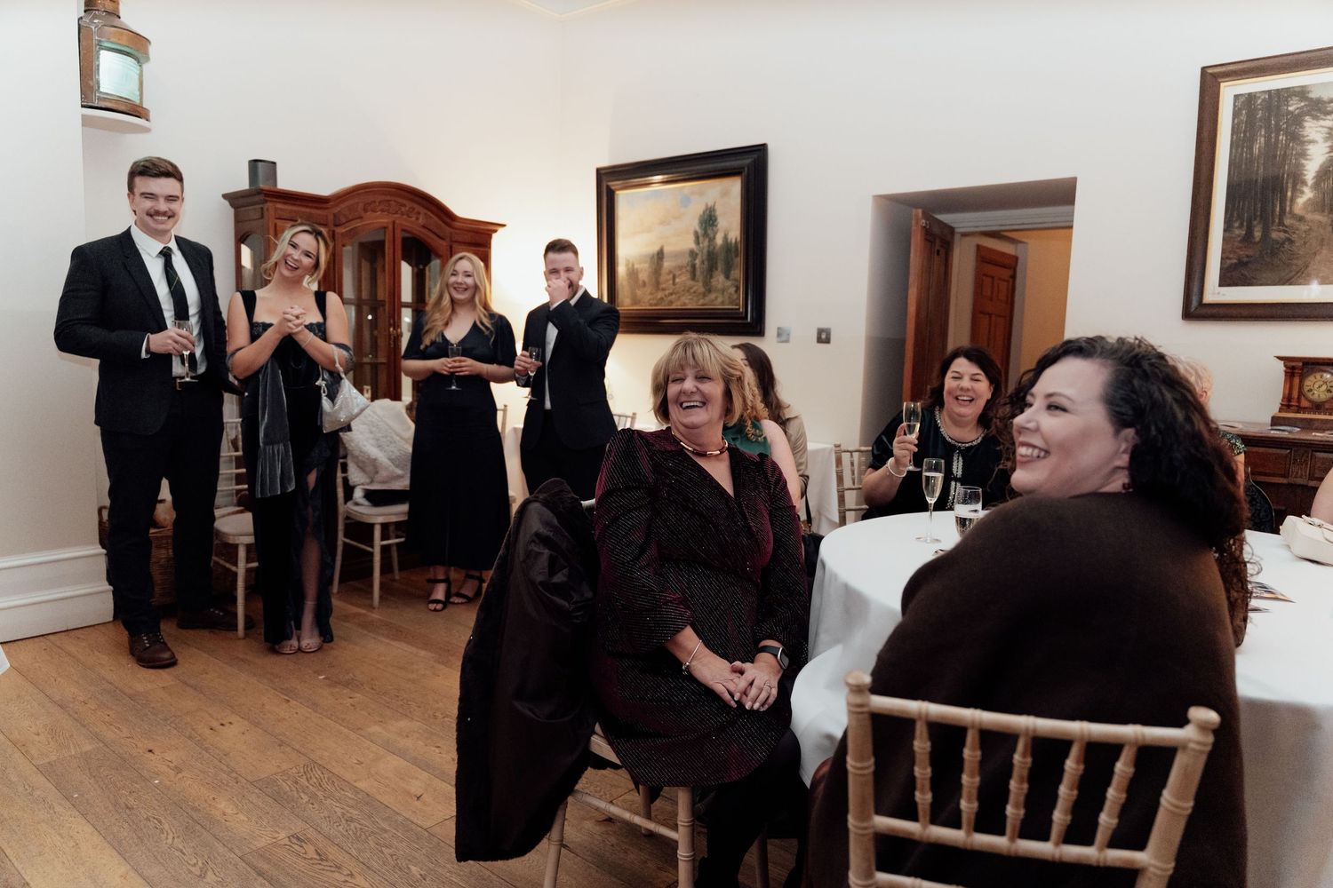 Event space with white walls and wooden furniture where guests are mingling.