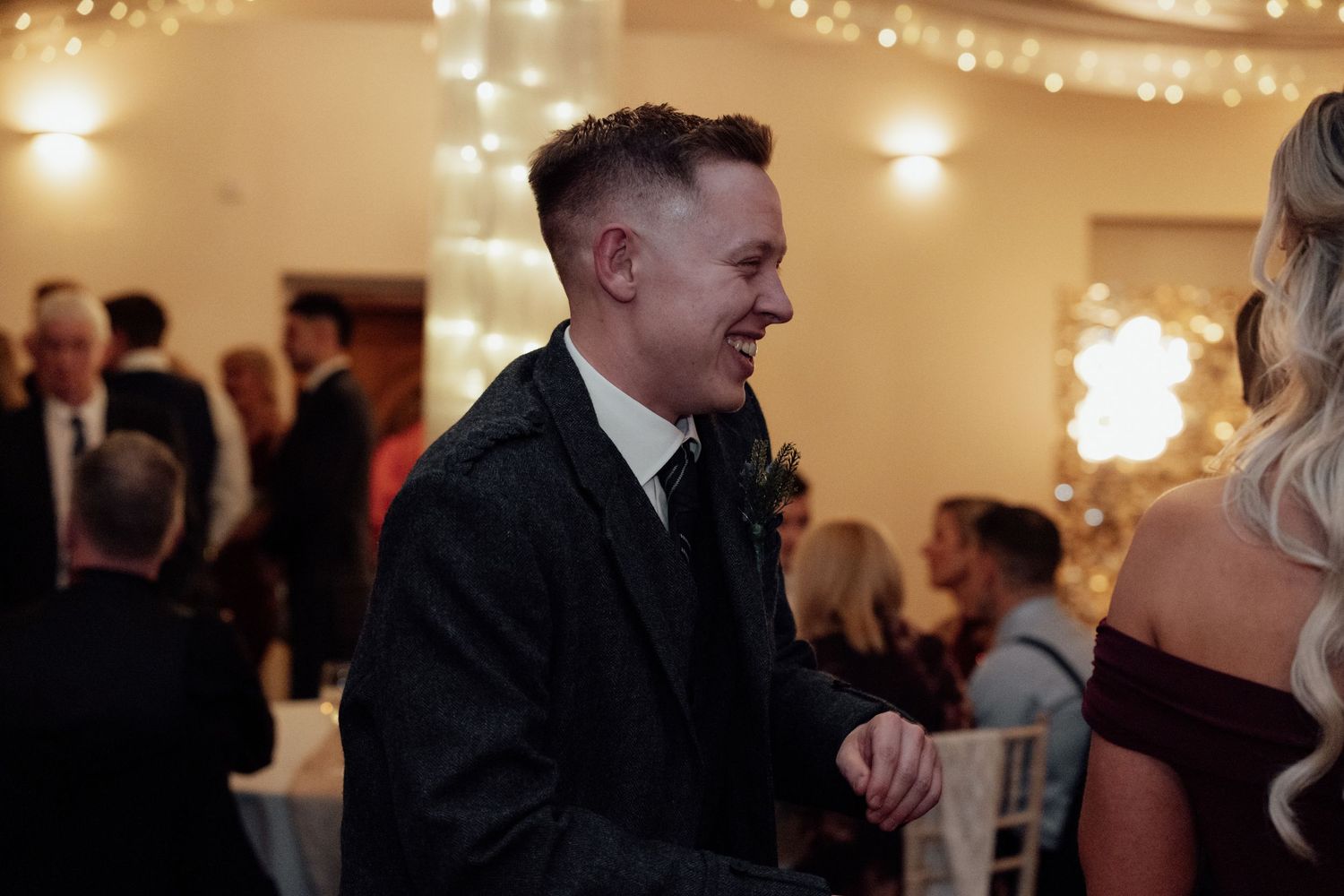 Lively conversation and laughter during an evening wedding reception with string lights in the background.