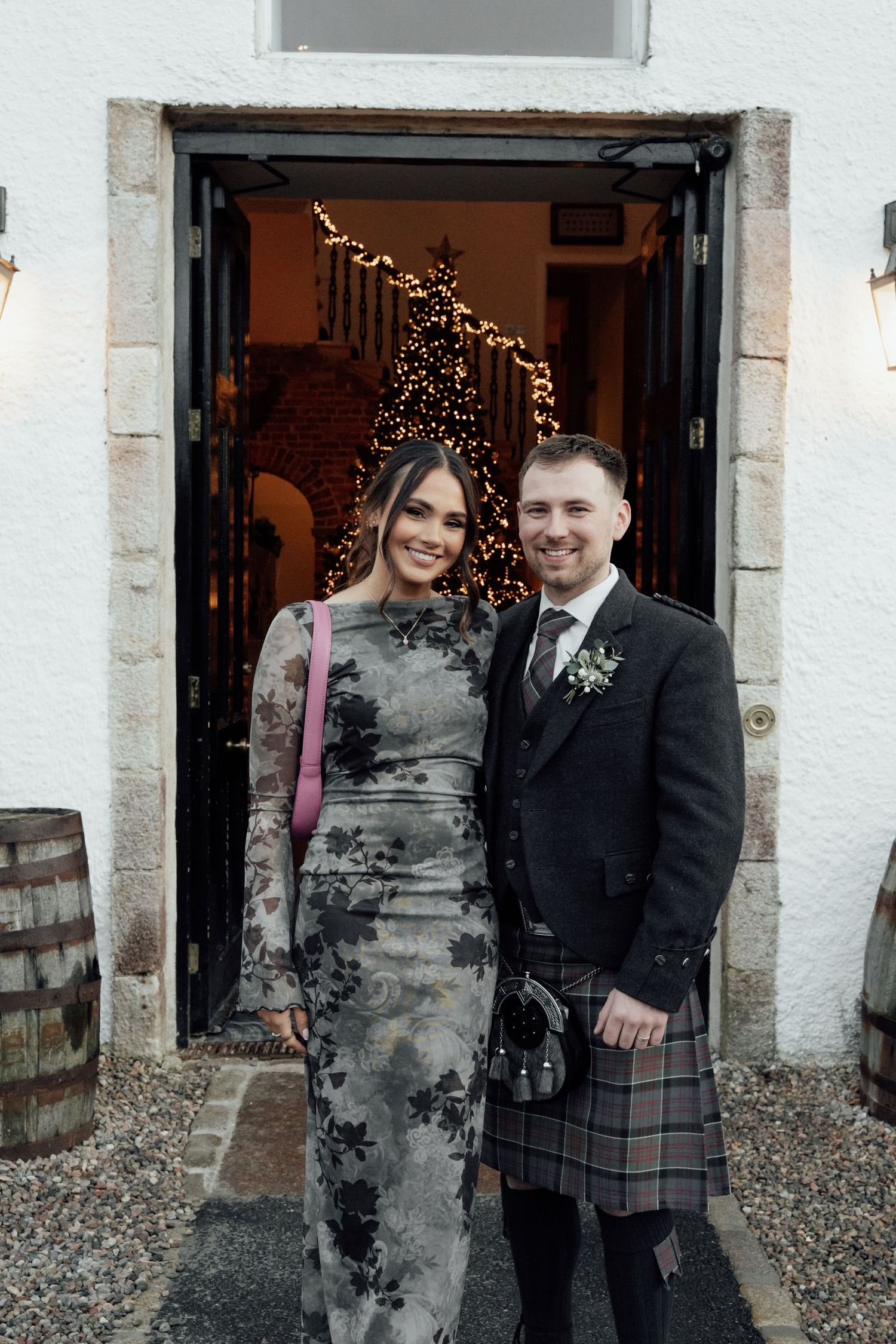 Wedding couple poses together outside a venue entrance with twinkling lights visible in the background.
