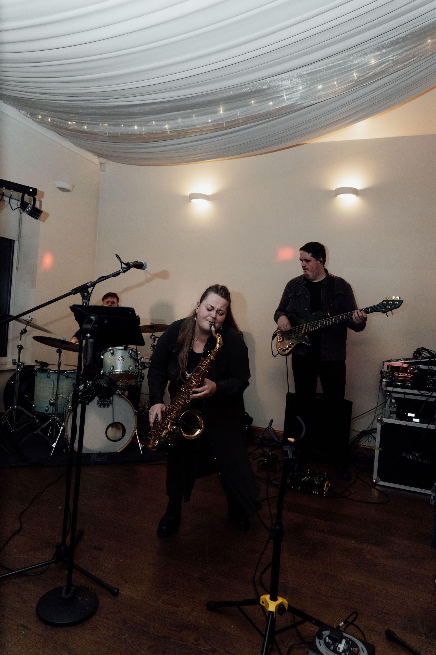 Band members perform on stage at a wedding reception with instruments and equipment setup.