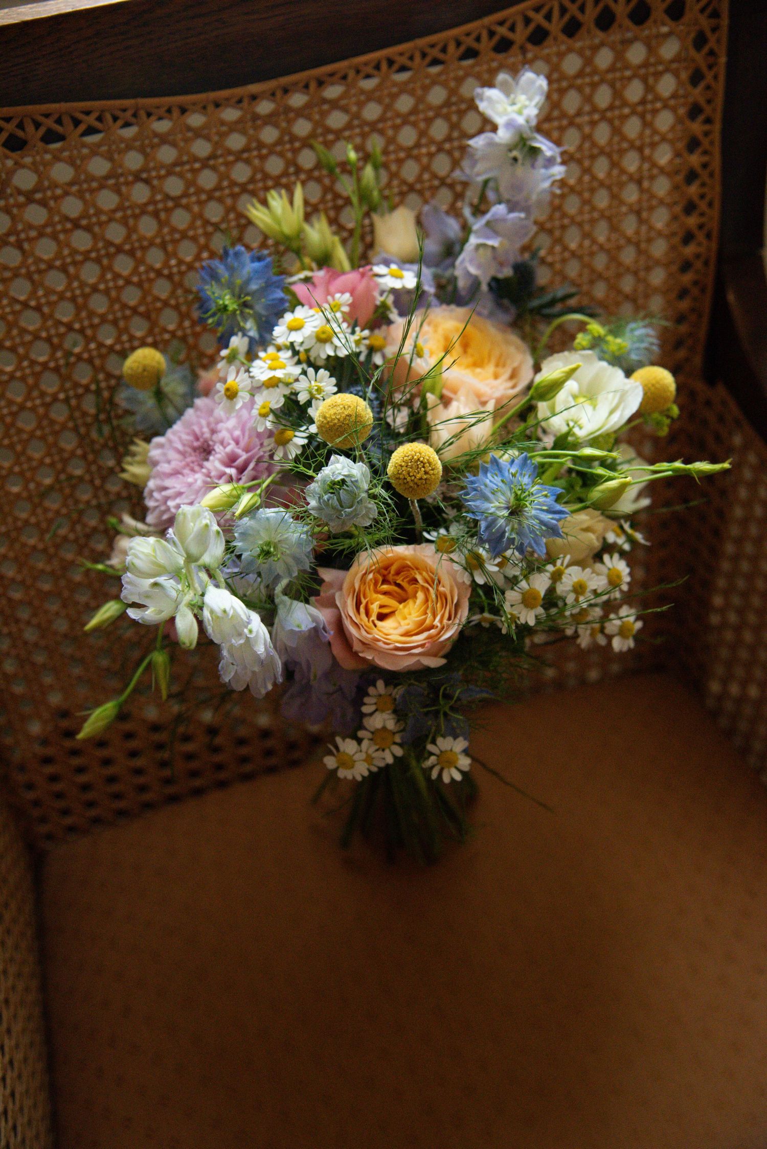 Colorful wedding floral arrangement with roses, daisies and blue flowers against a patterned backdrop.