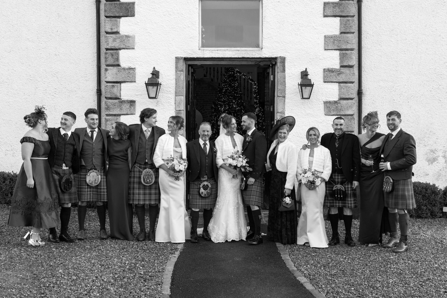 Black and white photo of wedding party lined up outside stone building entrance with lanterns.