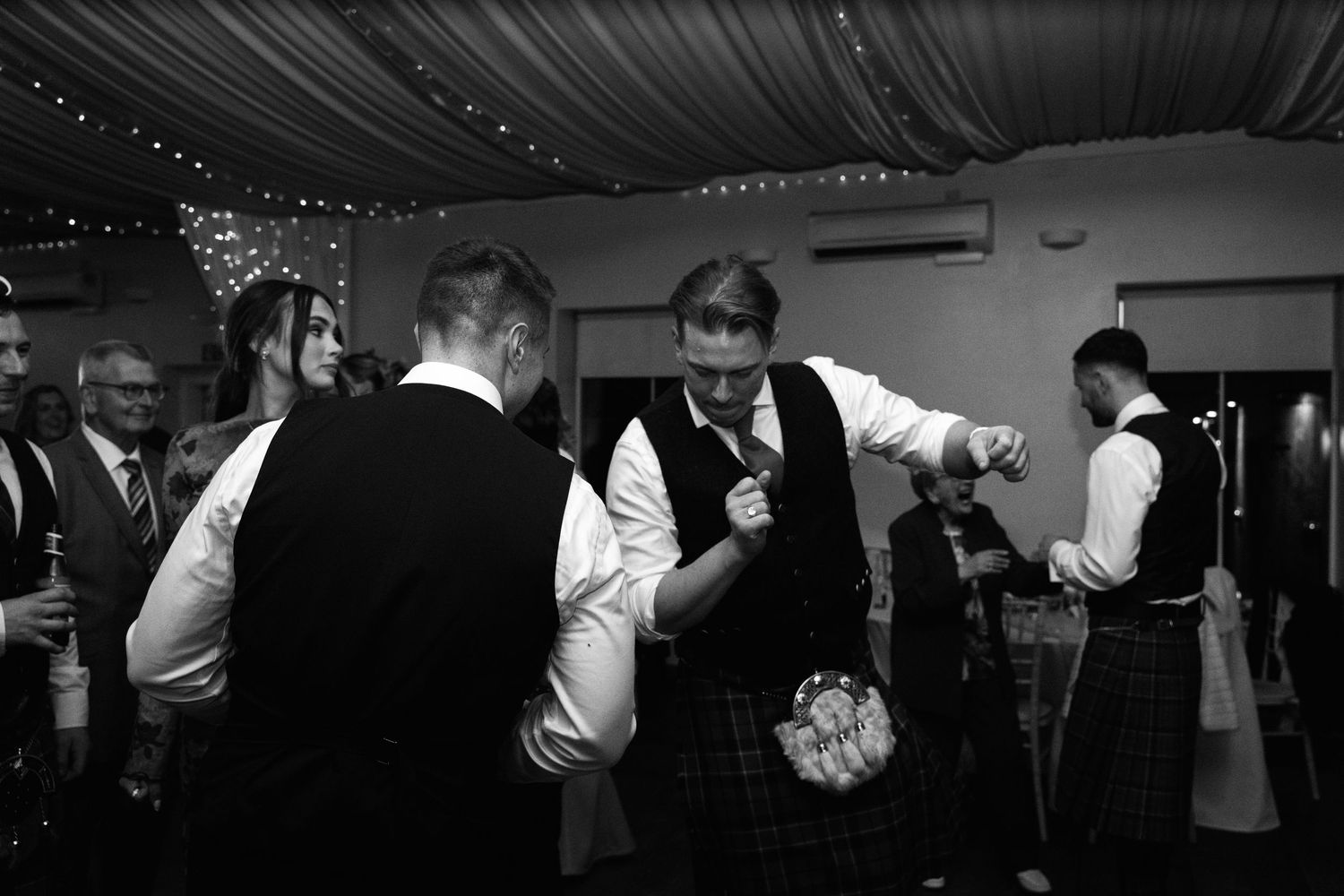 Black and white candid shot of guests interacting at an elegant indoor reception.