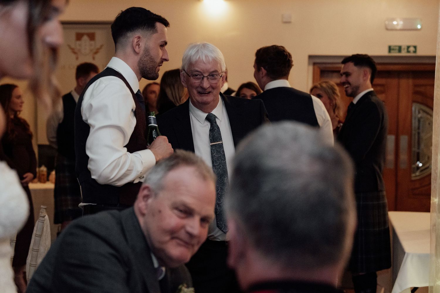 Wedding guests engage in conversation at an elegant indoor reception venue.