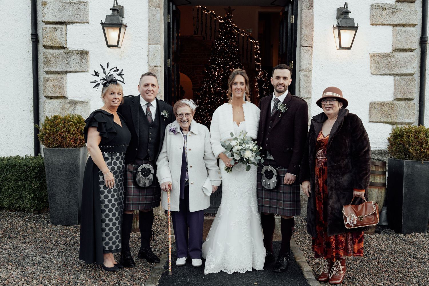 Extended wedding party gathering outside venue showing Scottish and formal dress combinations.