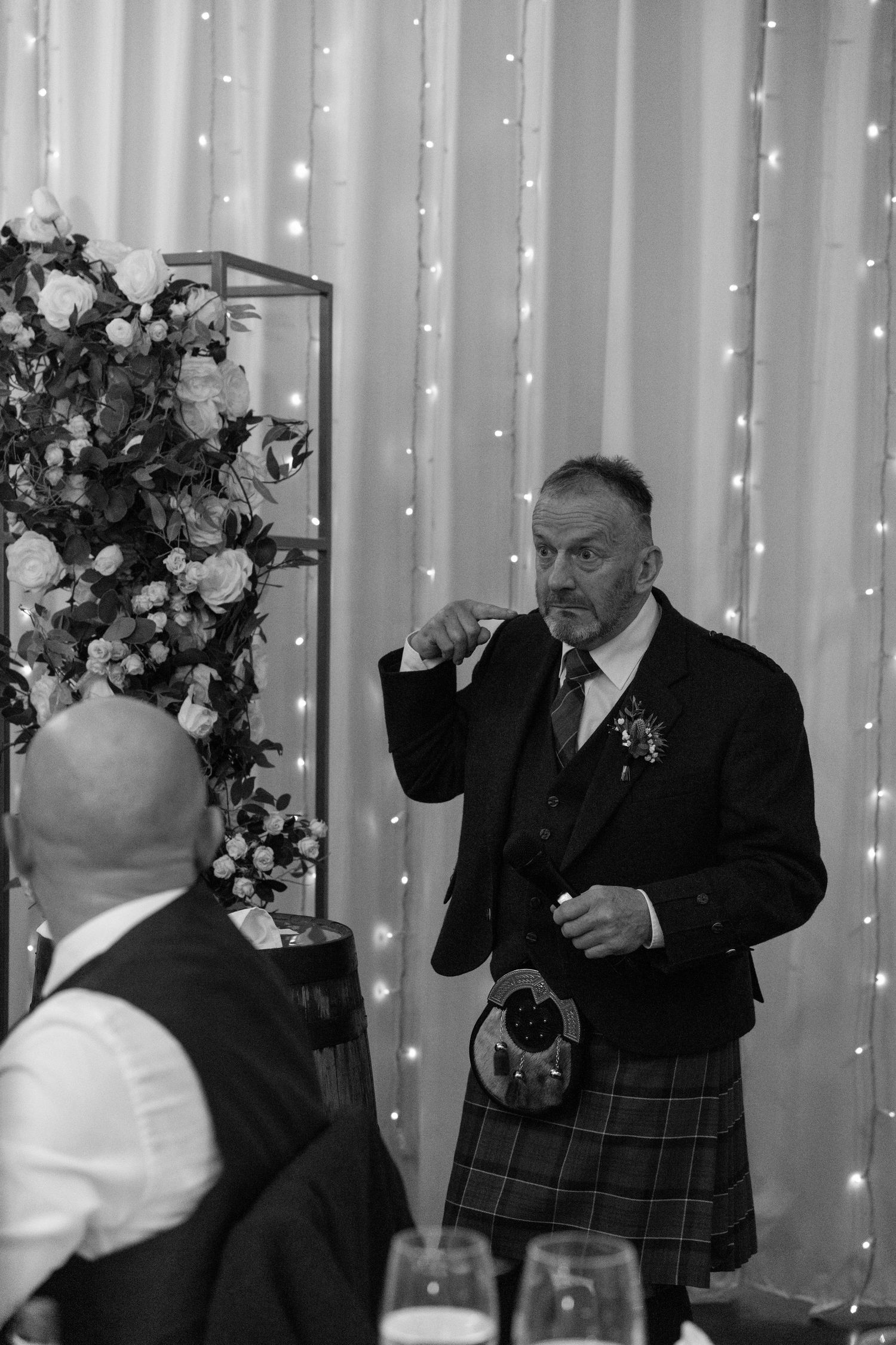 Wedding toast moment in front of twinkling light backdrop with floral decorations.