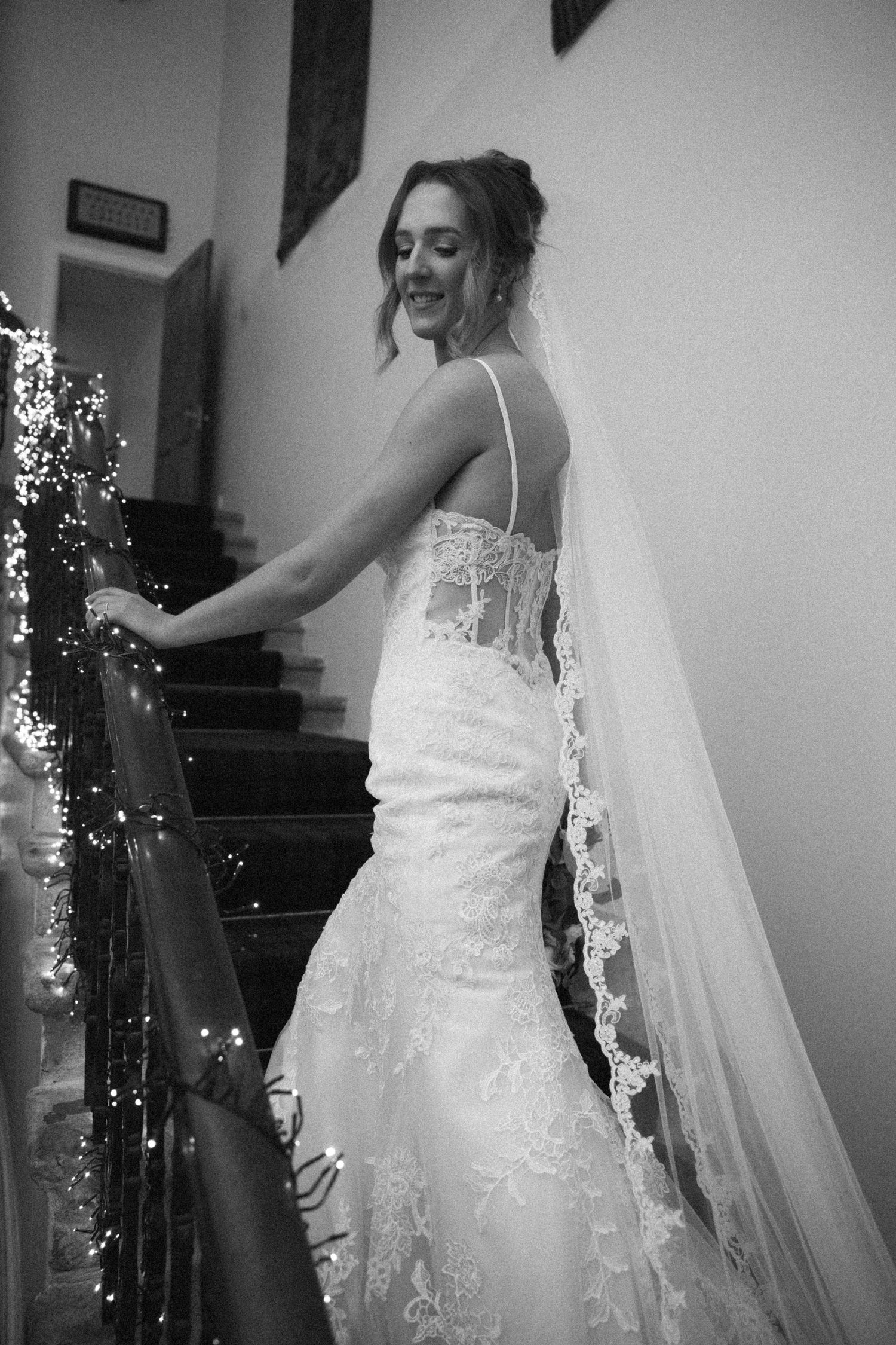 Black and white portrait of bride showing off her wedding dress near illuminated staircase.