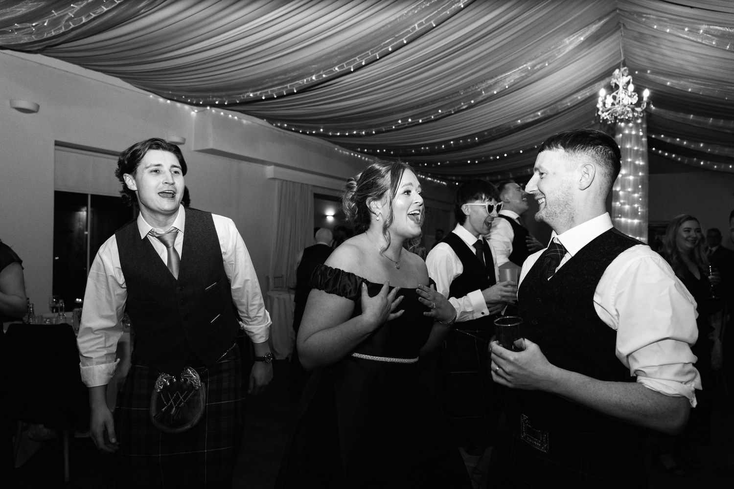 Black and white photo of wedding reception dancing with dramatic ceiling draping and lighting.
