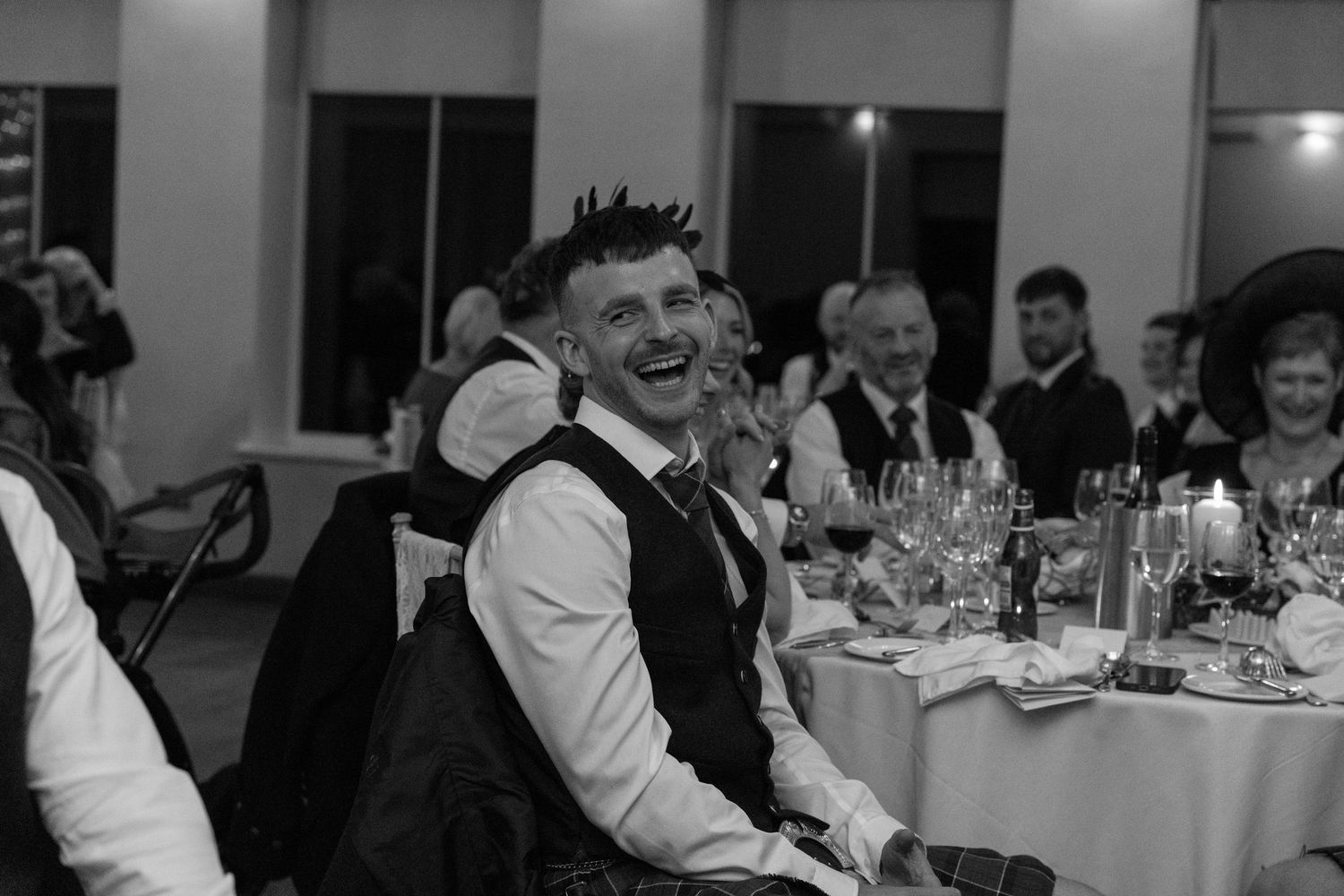 Wedding reception guests seated at decorated tables enjoy dinner and conversation in an elegant indoor venue.