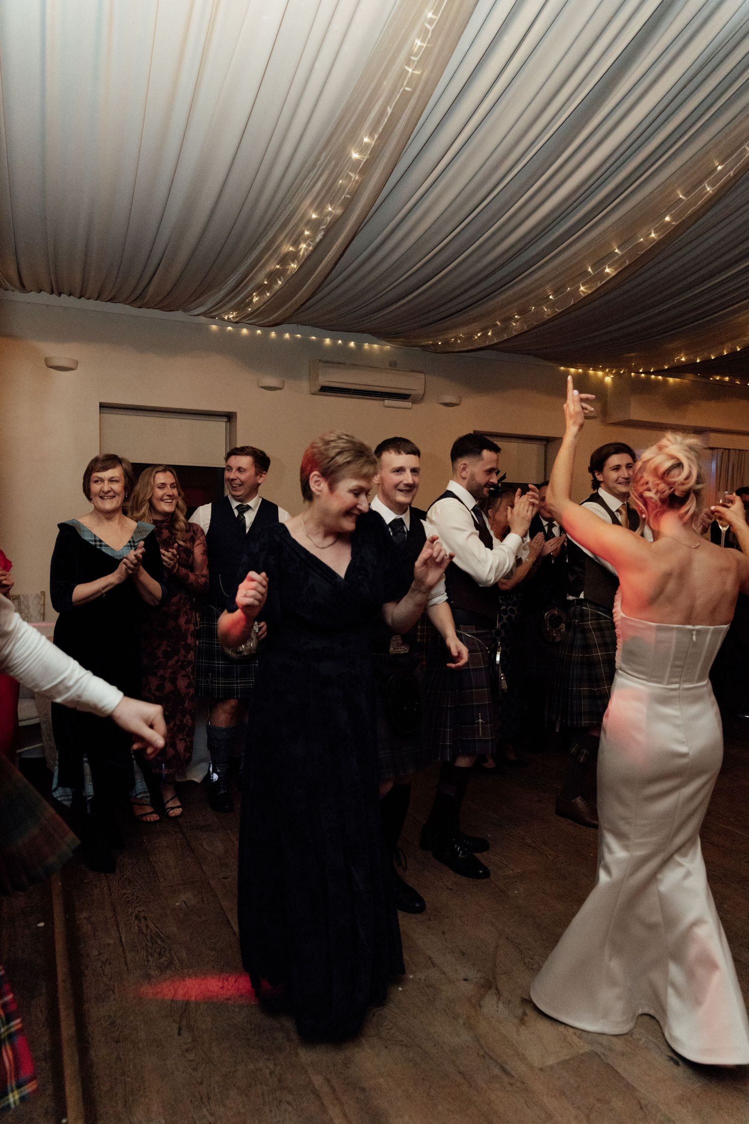 Energetic wedding reception dance party with guests celebrating under draped ceiling decor.