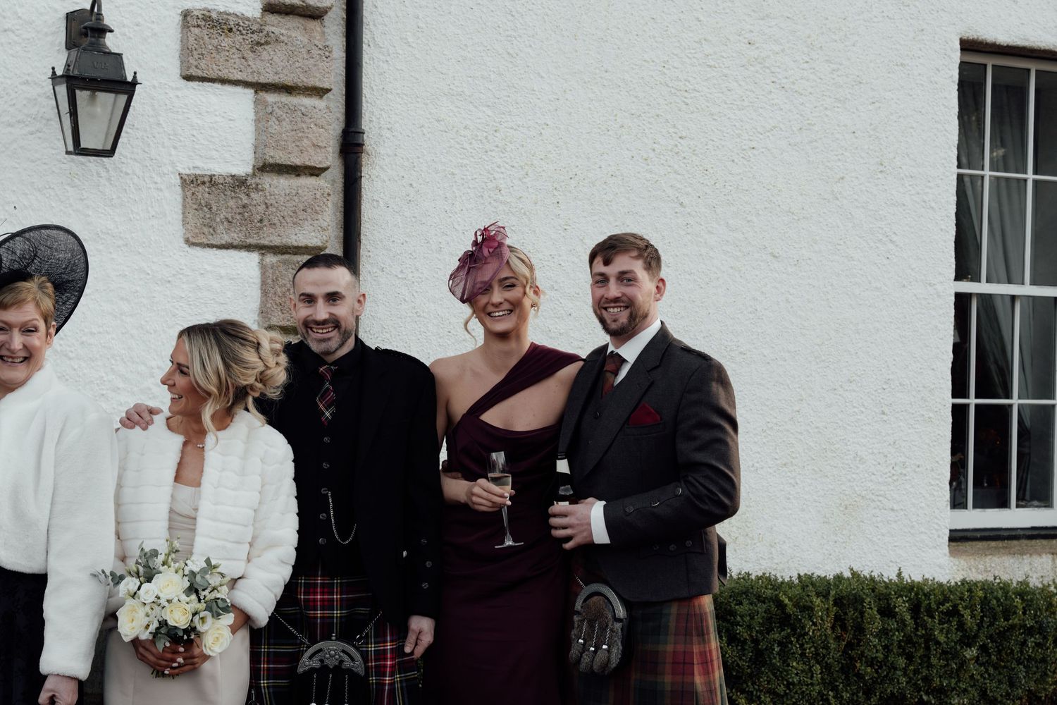 Casual wedding group photos taken outside white stone building with traditional architecture.