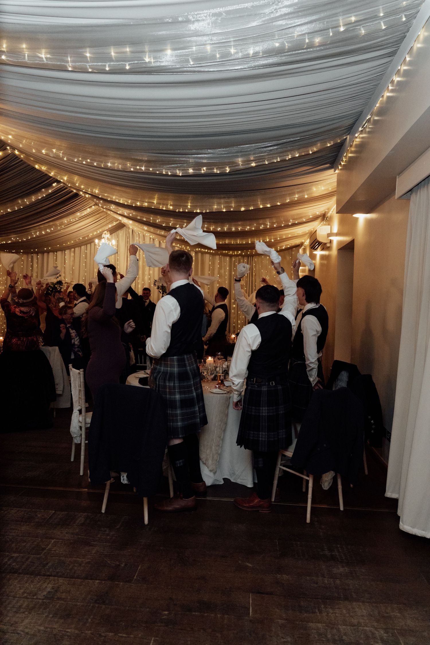 Wedding reception in an elegant white-draped venue with twinkling lights and wooden flooring.