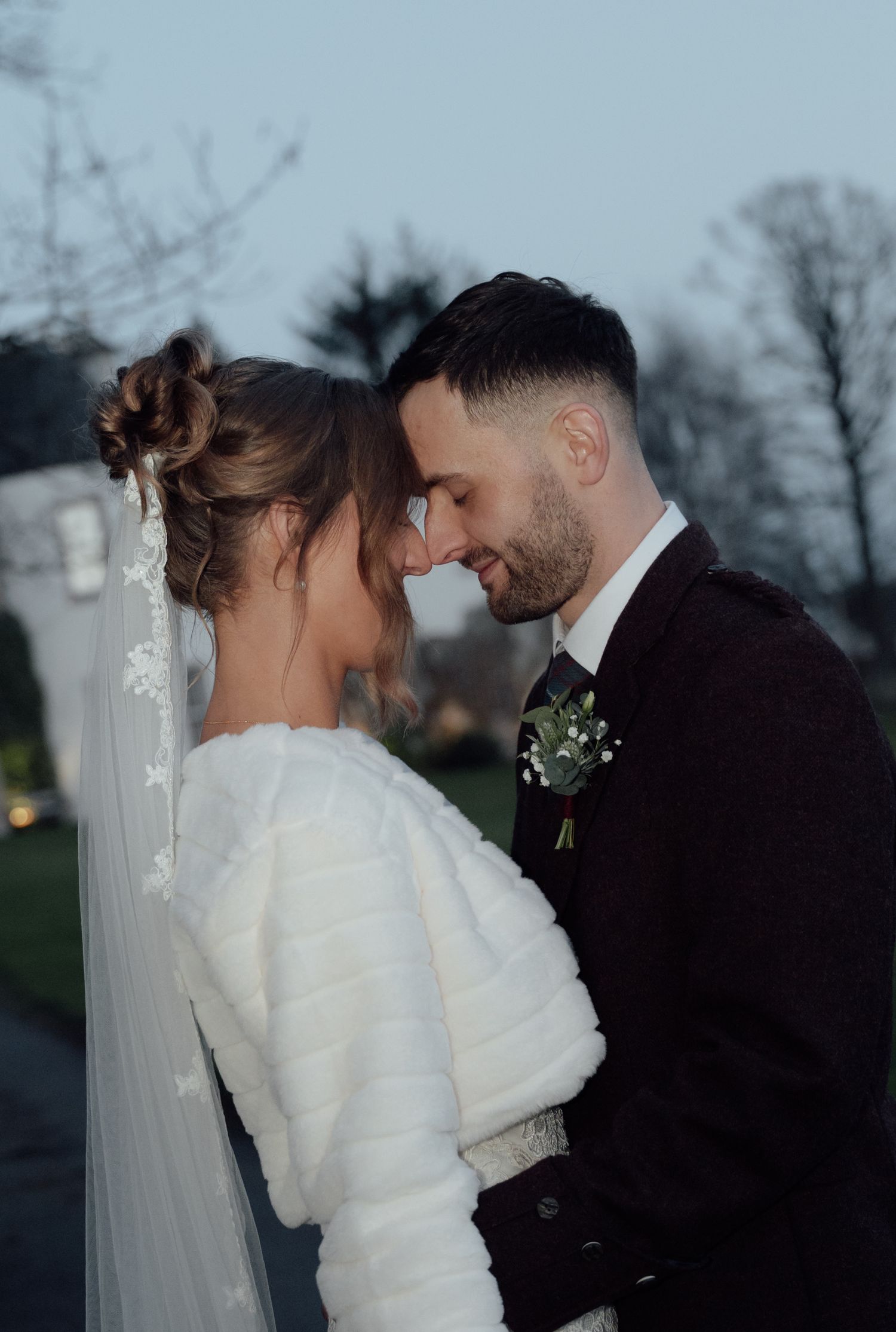 Intimate wedding portrait of couple in winter attire sharing a close moment outdoors.