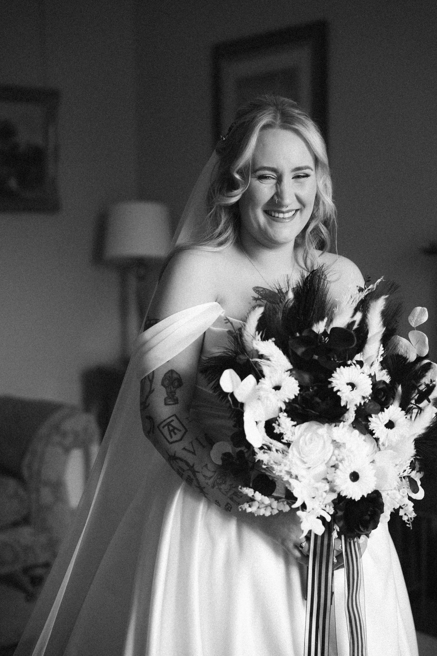 Black and white photo of a laughing bride in a strapless gown holding a large floral bouquet with veil.