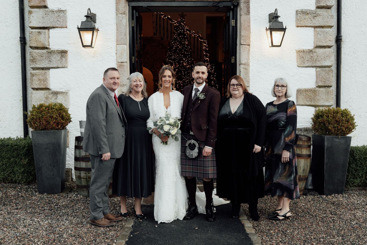 Wedding party members gather outside a white stone building with lantern decorations.