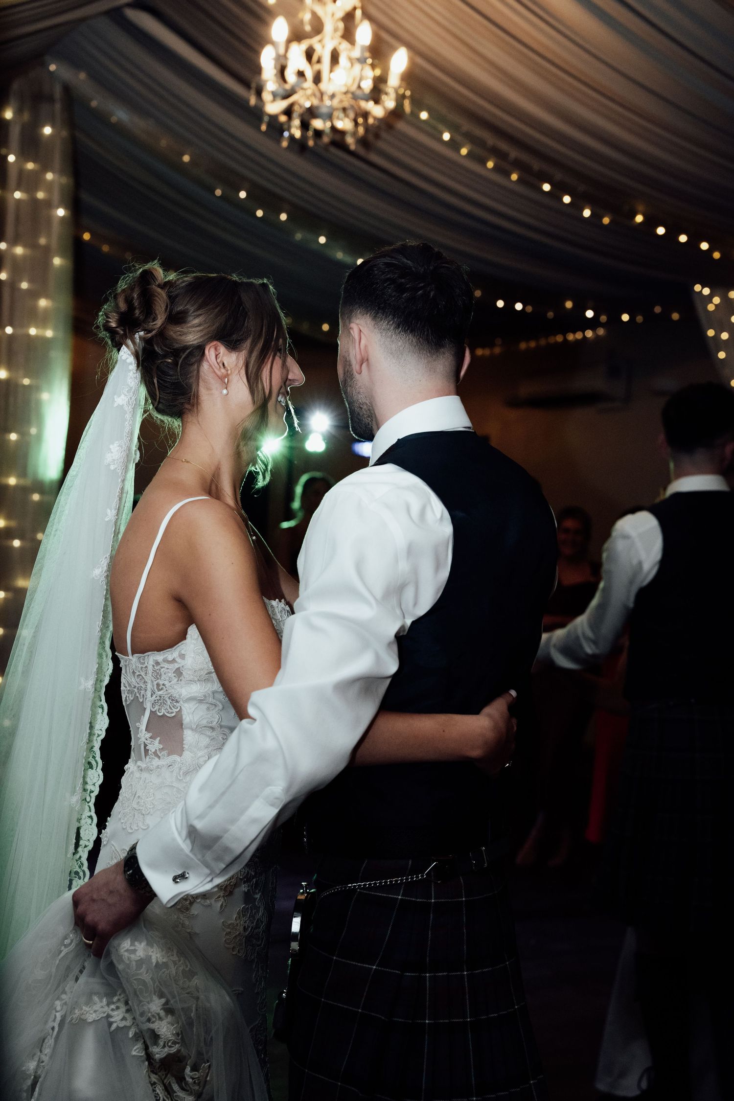 Newlyweds dancing together under twinkling lights and draped fabric at their reception.