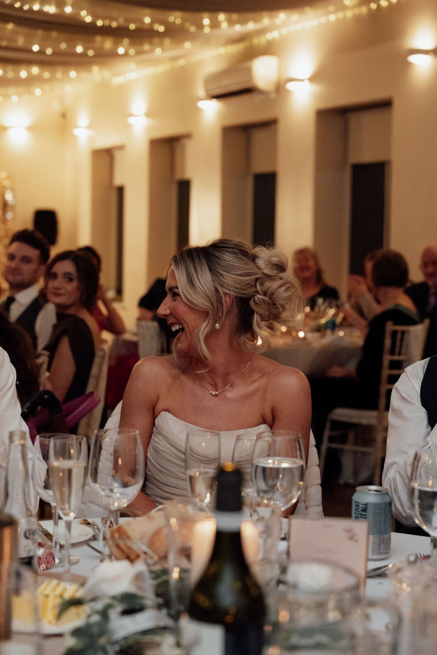Elegant wedding reception with guests dining under string lights and warm lighting.