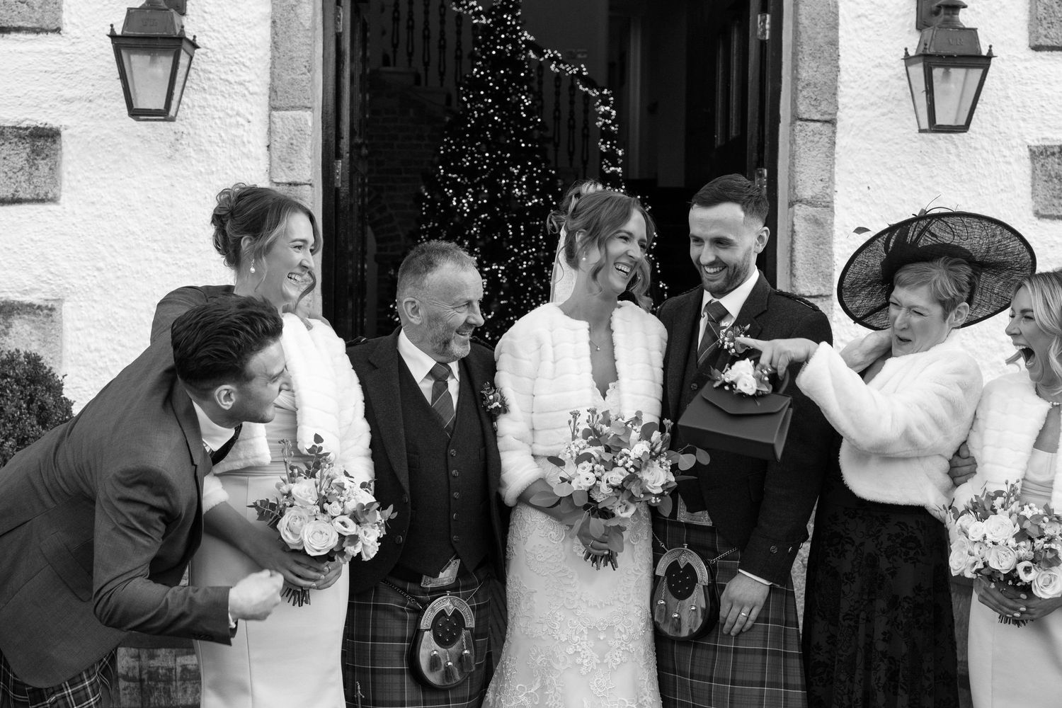 Joyful wedding celebration outside historic building with Scottish dress elements.